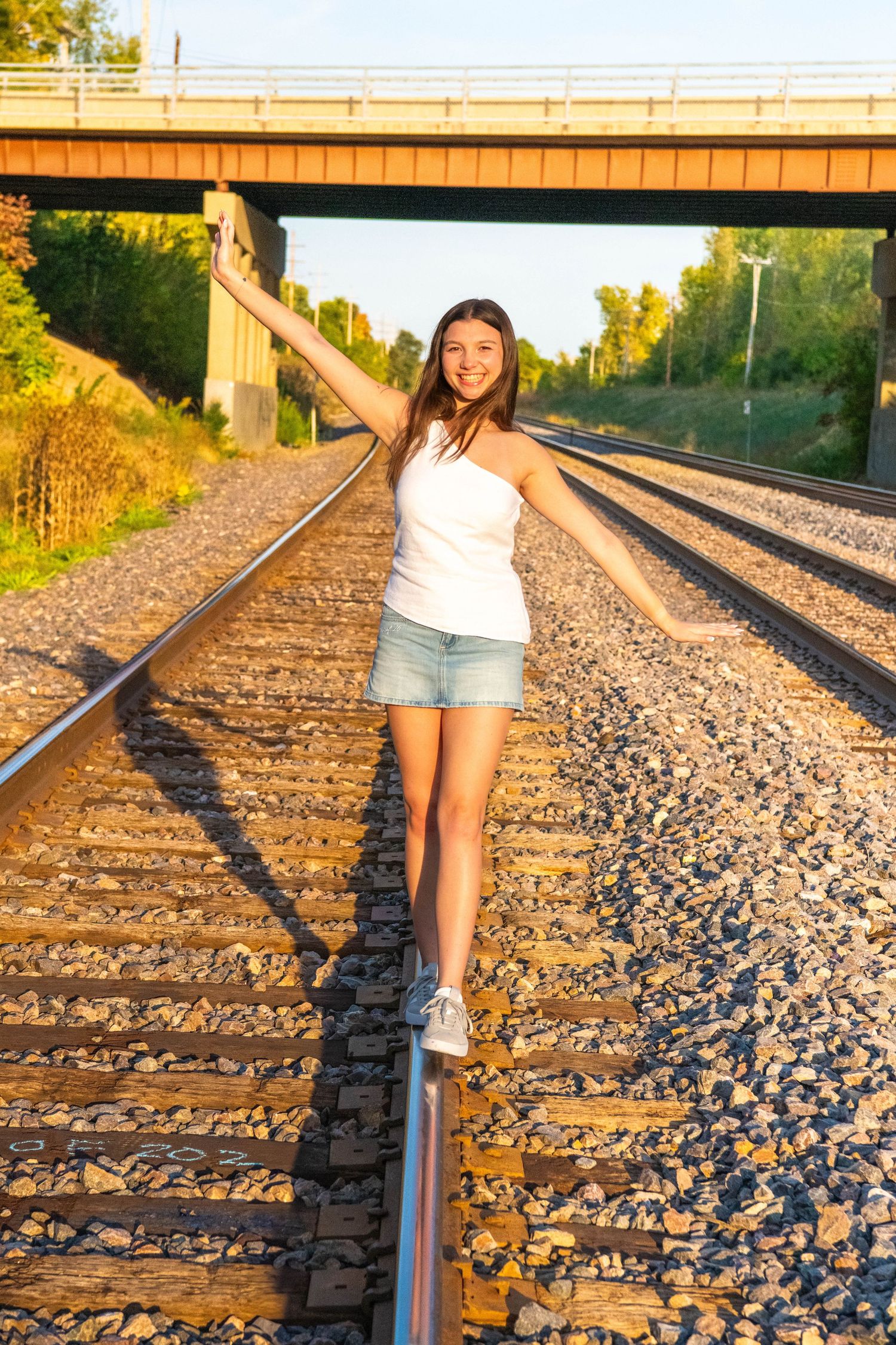 Railroad tracks stretch into the distance during golden hour as someone walks along the rails in summer.