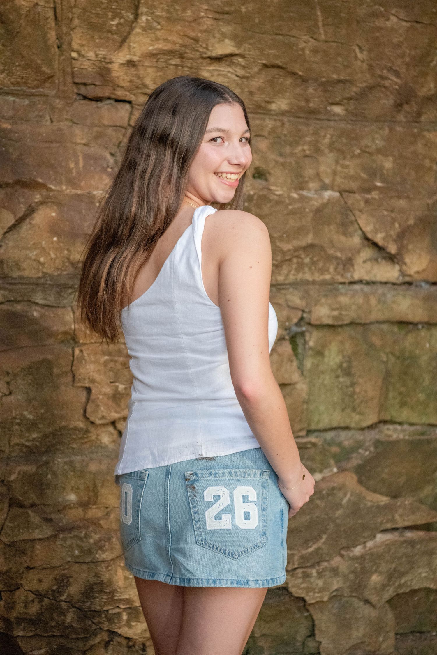 A series of photos showing a person in a white tank top and denim shorts posing against a rustic stone wall.