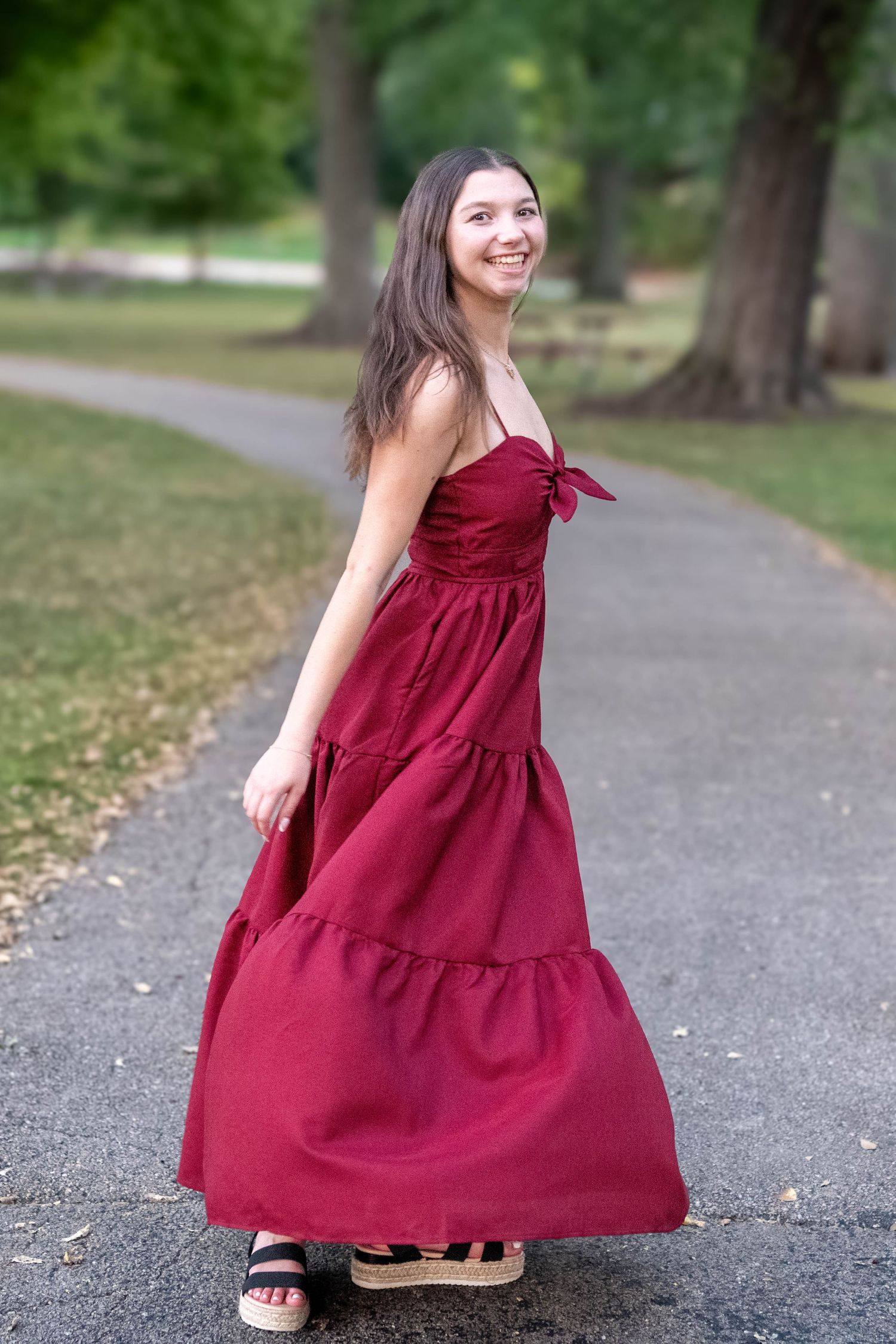 A sequence of photos showing someone twirling in a flowing burgundy dress on a tree-lined path.