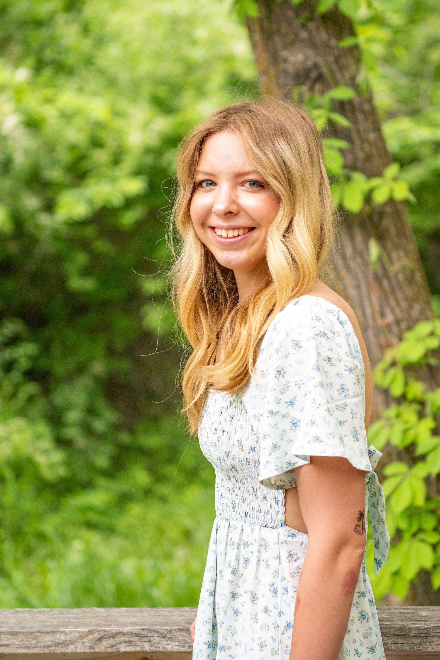 A white floral dress contrasts beautifully with lush green foliage in a summer outdoor portrait.