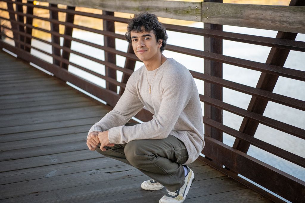 Person in light sweater crouching on wooden boardwalk with railing.