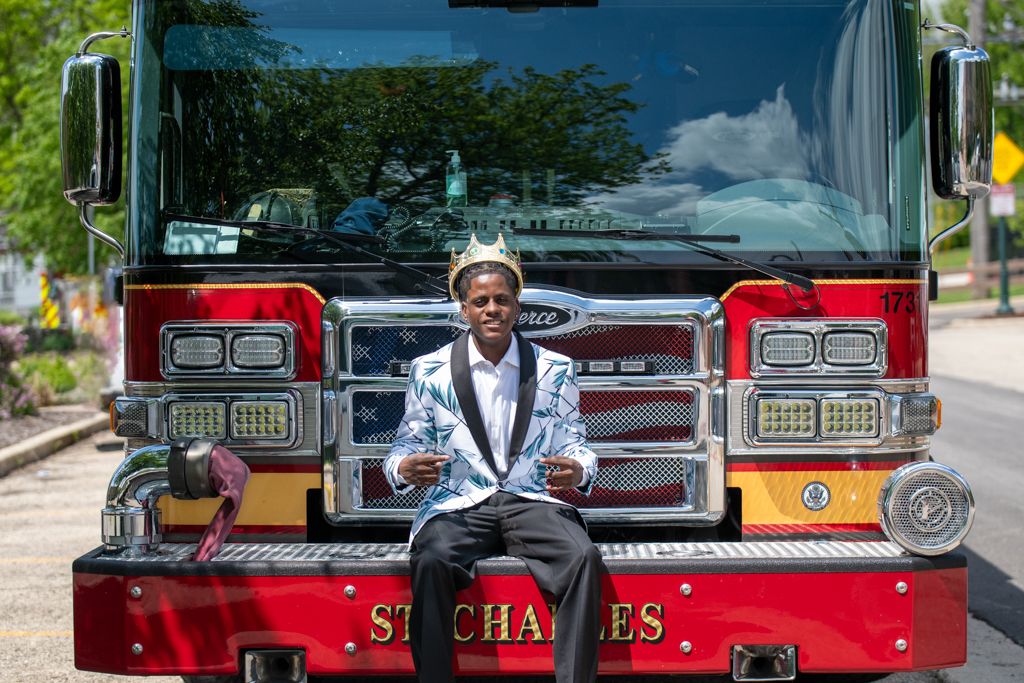 A person in formal attire stands in front of vintage red fire trucks.