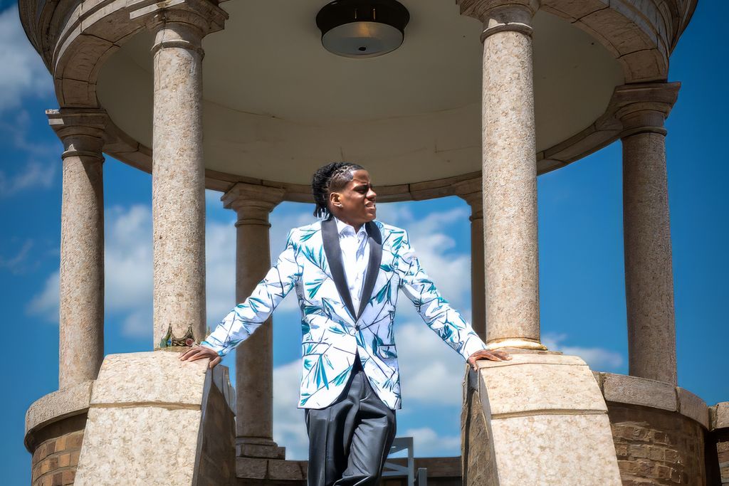 A person in a white and blue blazer poses in a classical columned gazebo structure.