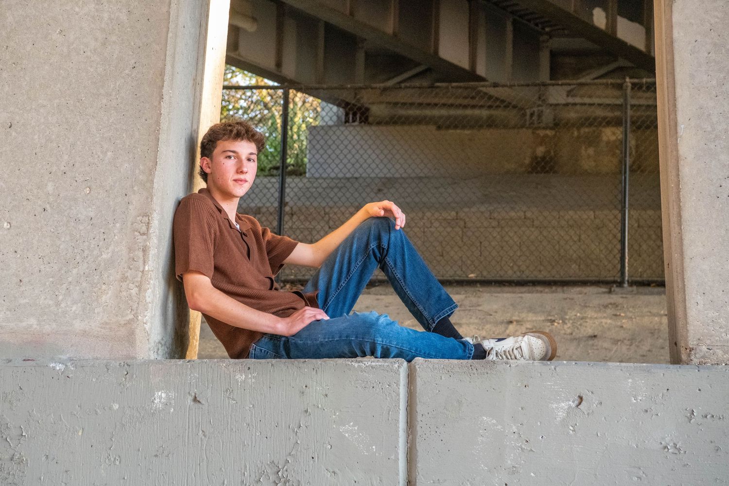 Person in casual attire sits on a concrete ledge in an industrial or abandoned setting.