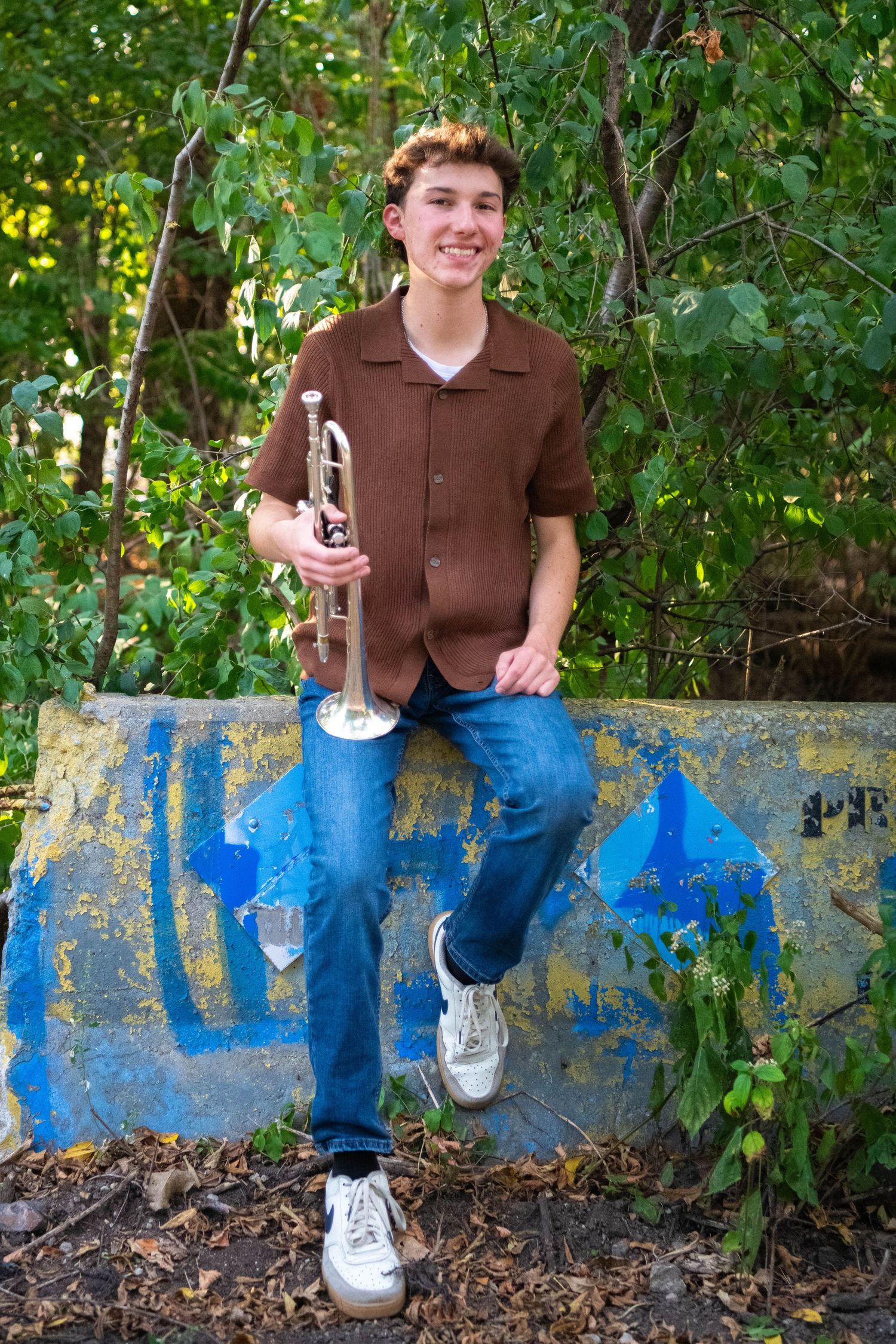 A series of four casual outdoor portraits showing someone sitting on a blue painted concrete wall among green foliage.