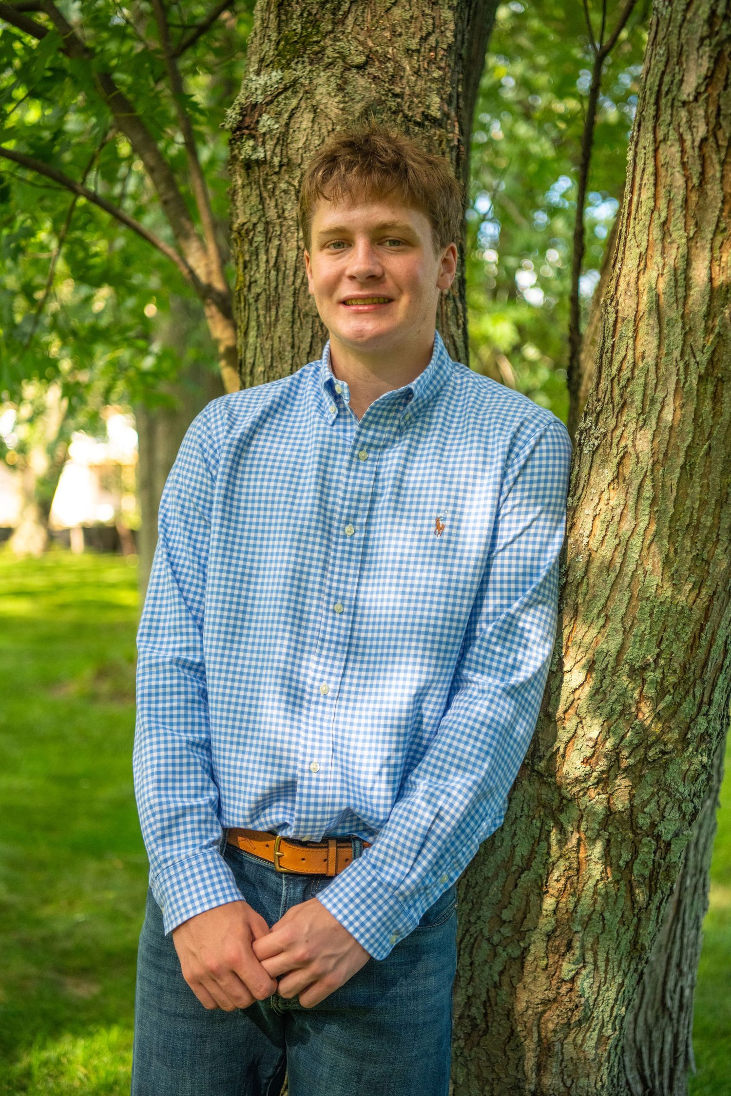 A series of outdoor portraits against a tree trunk with green foliage in the background, wearing blue gingham shirt.