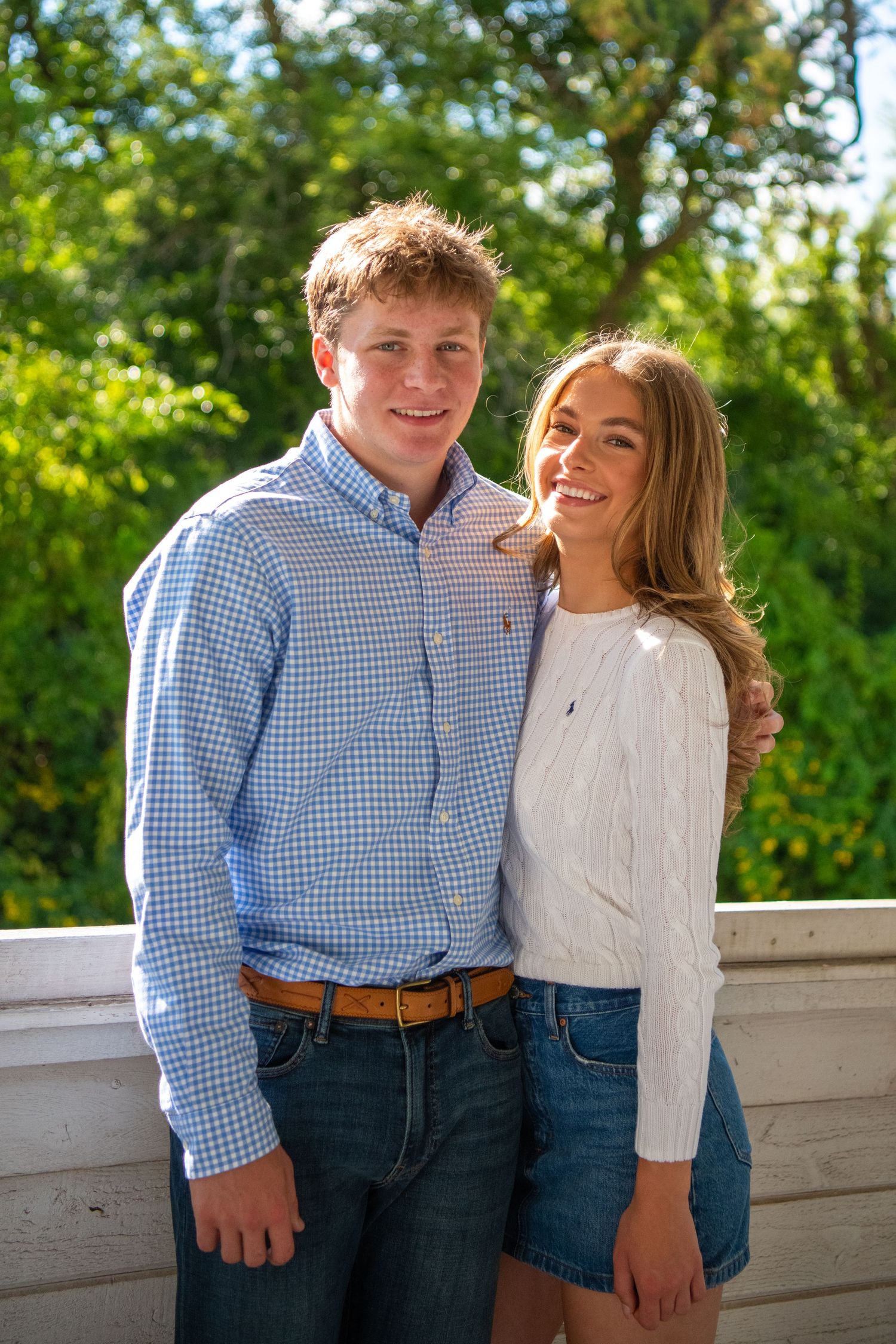Two people in coordinating blue and white outfits pose together outdoors on a sunny day.