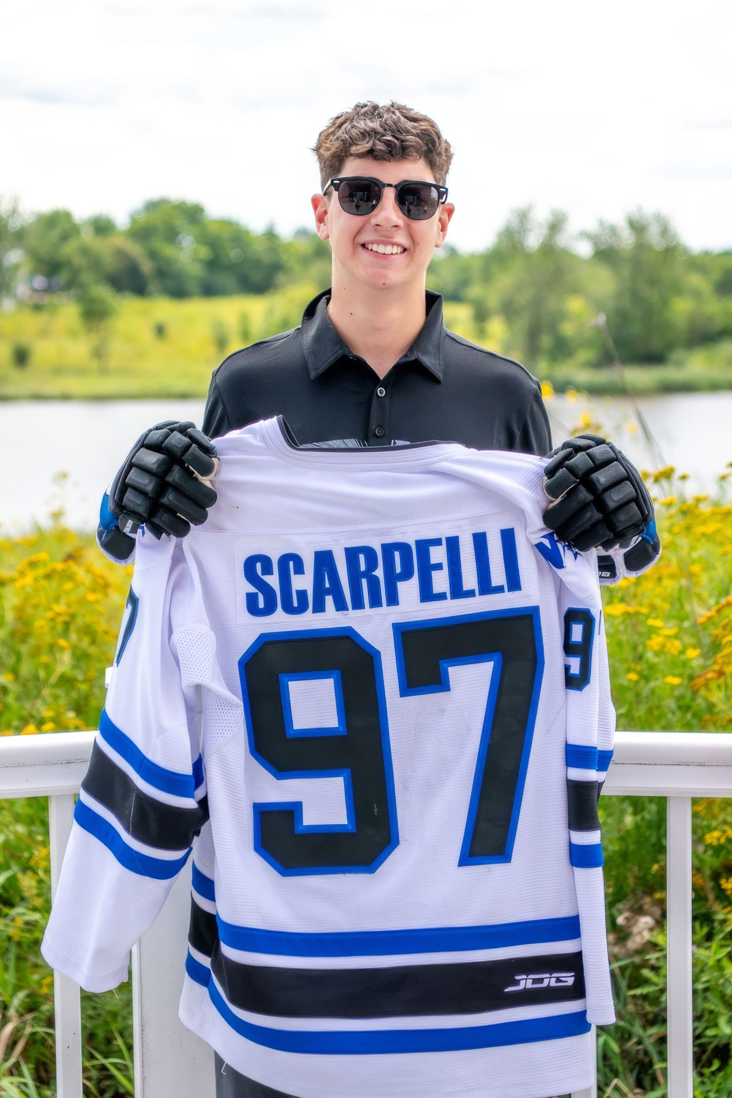 Person holding up white hockey jersey with number 87 outdoors near yellow flowers.