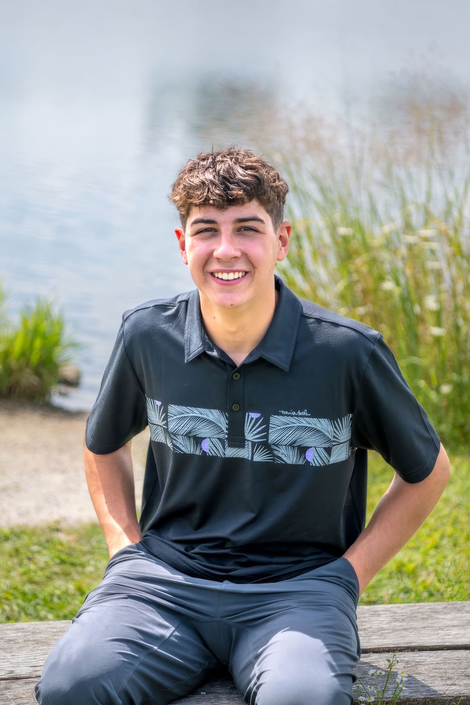Young person in black polo shirt sitting outdoors on a sunny day.