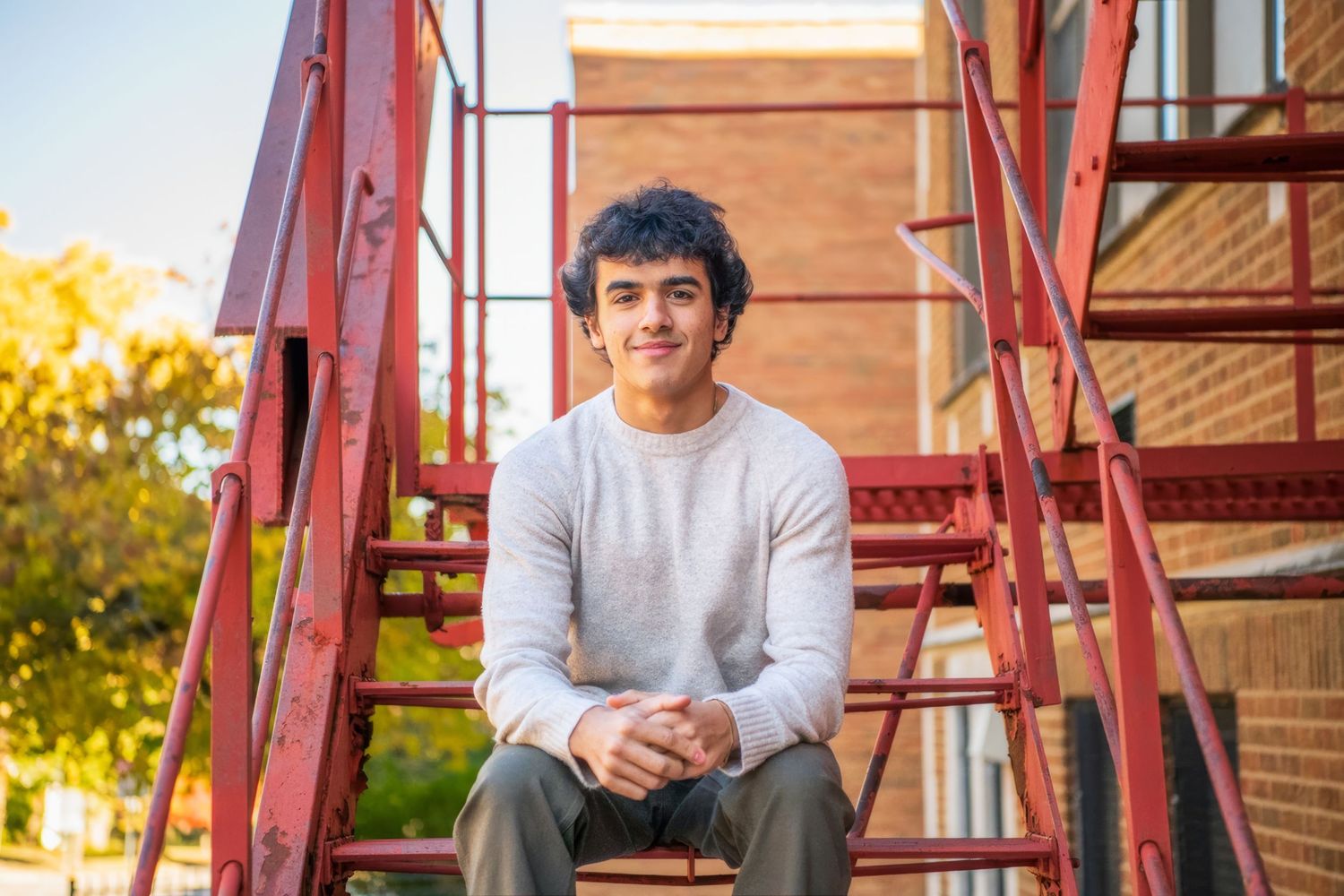 Person in gray sweater sitting on red metal stairs outdoors during autumn.