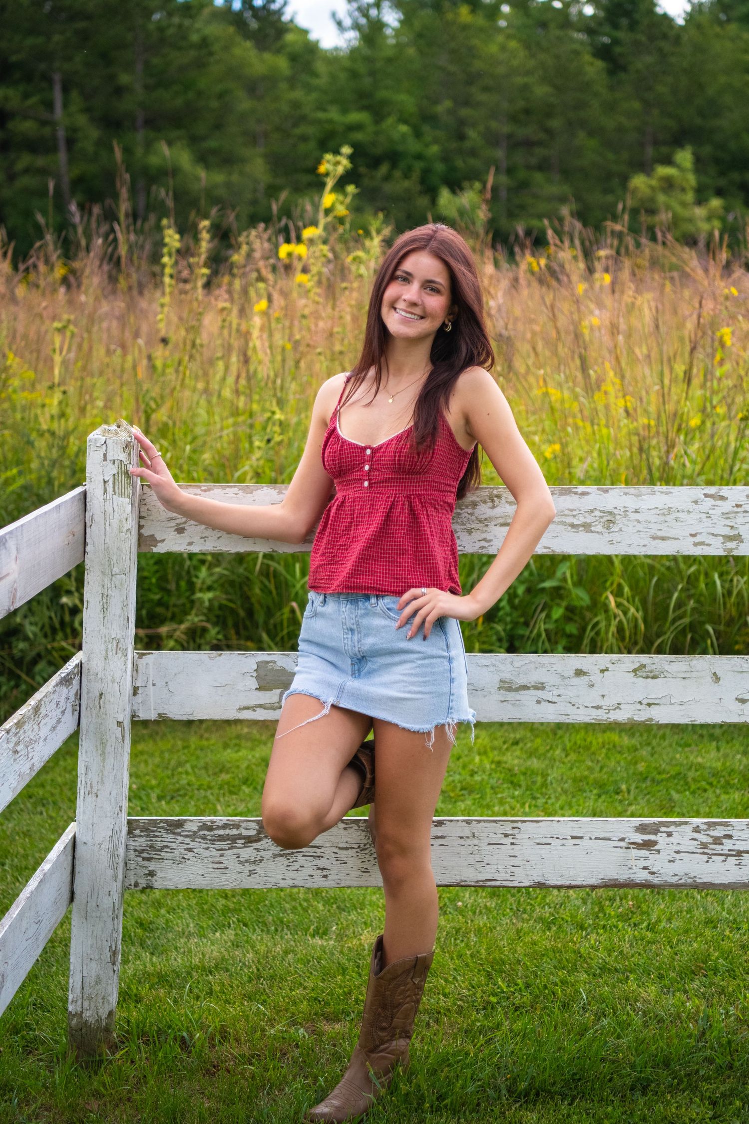 A scenic photoshoot with a rustic white wooden fence and tall grass in the background on a sunny summer day.