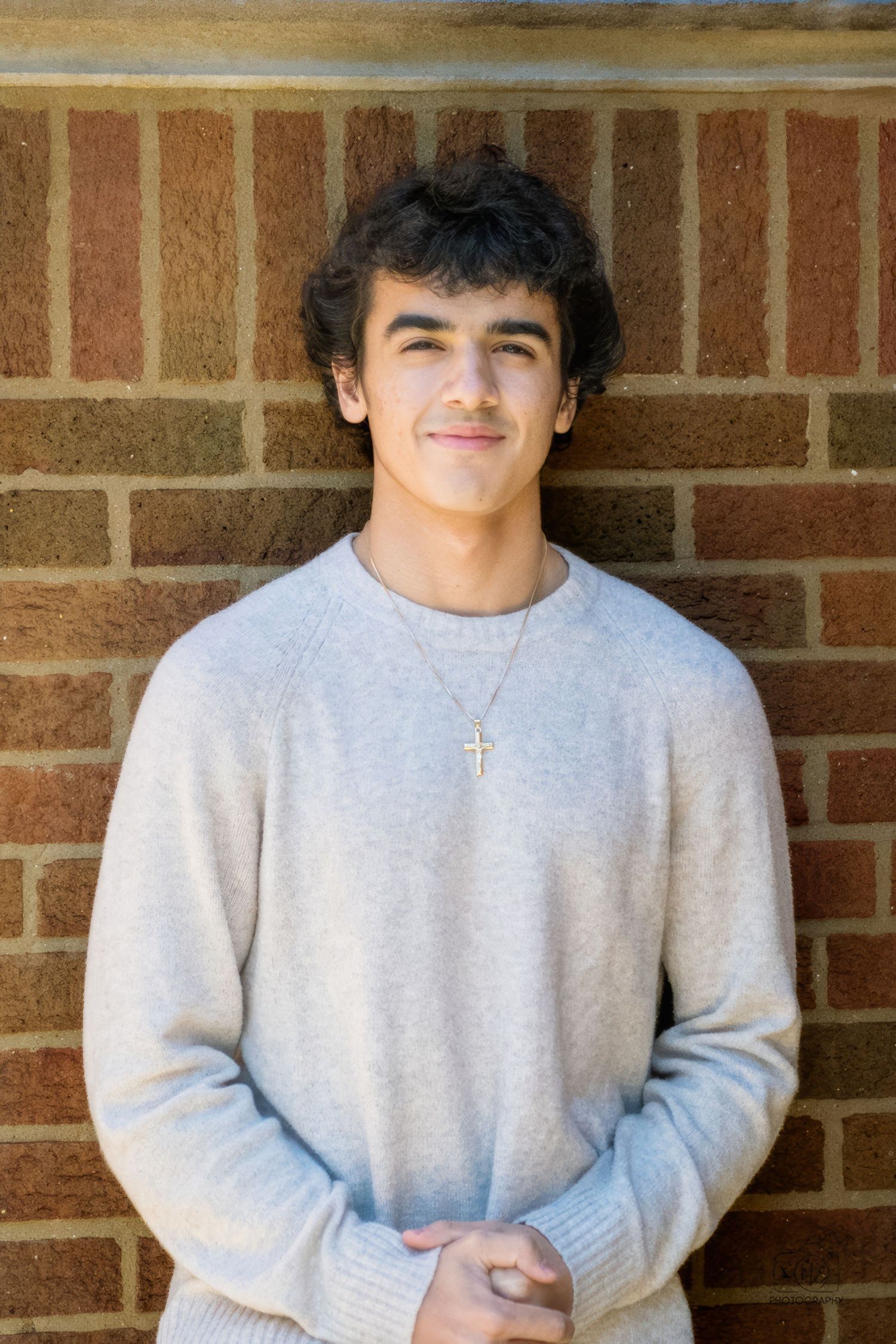 Person in gray sweatshirt standing against brick wall background.