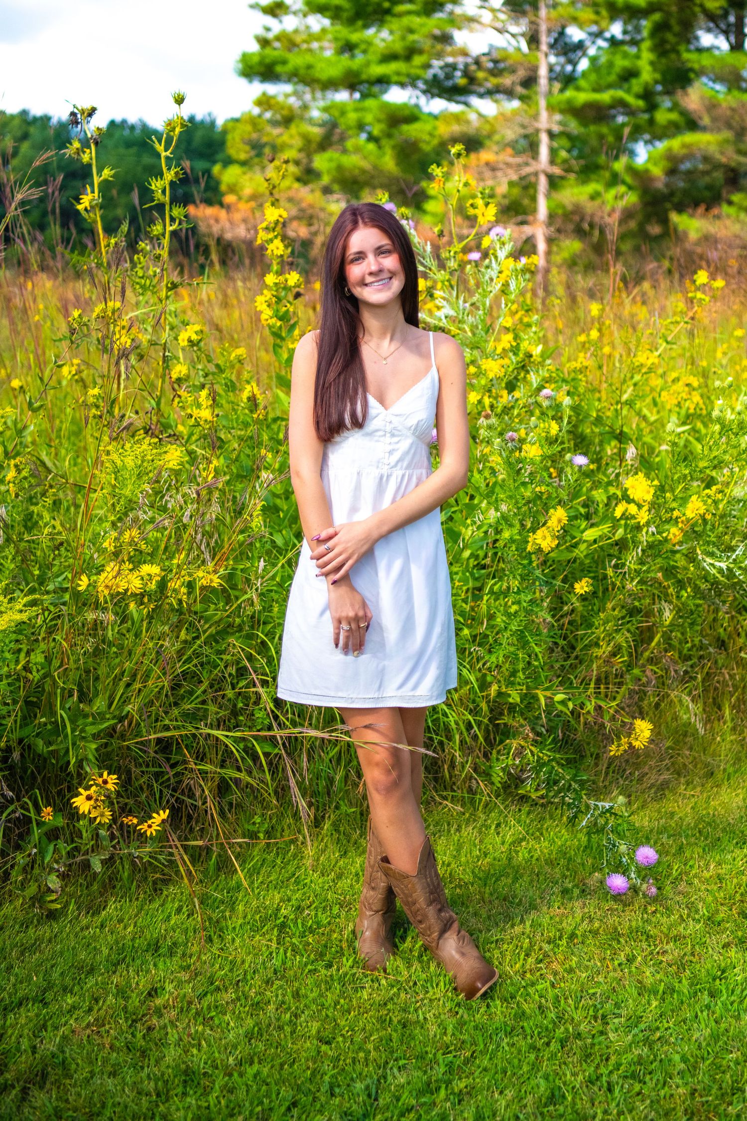 Person in white summer dress and brown boots standing in a wildflower meadow with yellow blooms and green grass.
