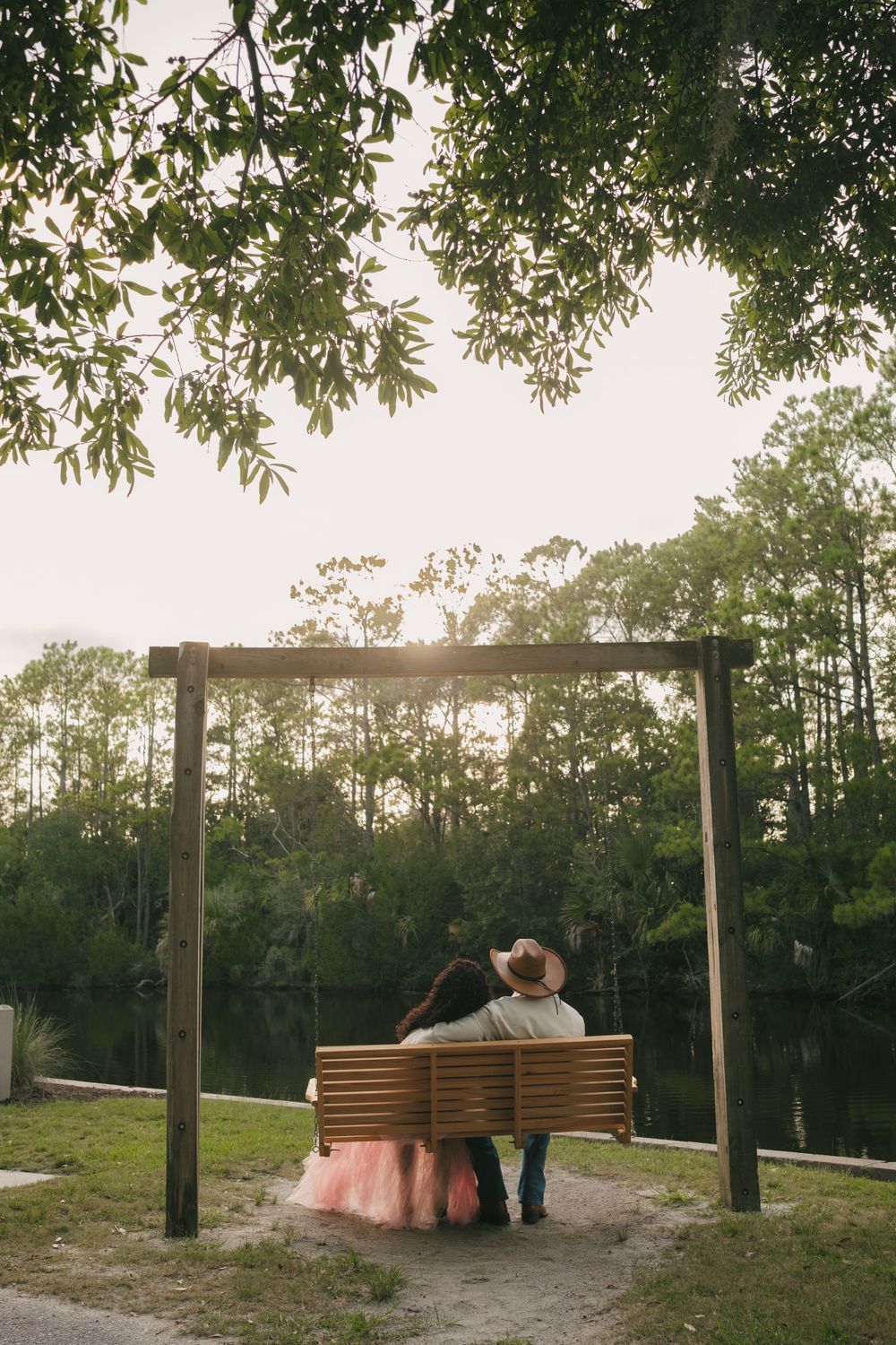 Charleston County Park session of a couple sitting on swing in cowboy-inspired outfits