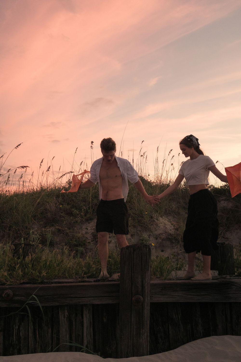 Couple holding hands and walking along the shoreline at Charleston’s Folly Beach during a golden sunset photography session.