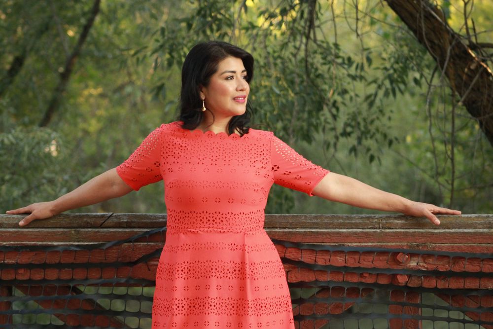 Person in coral dress poses against rustic railing in garden setting.