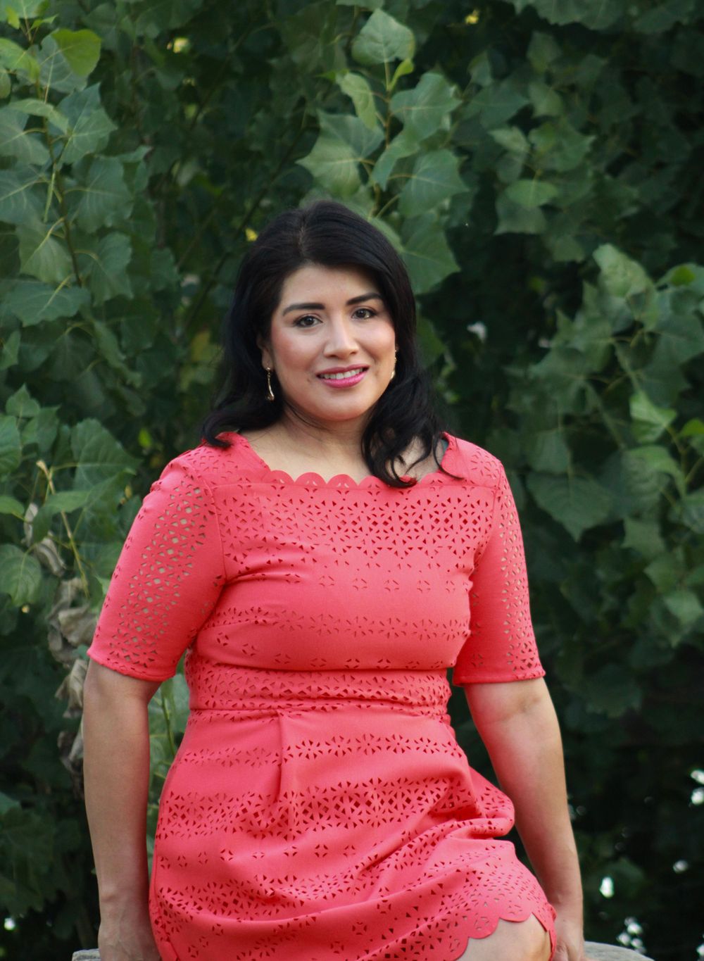 Portrait of person in coral eyelet dress against green foliage background.