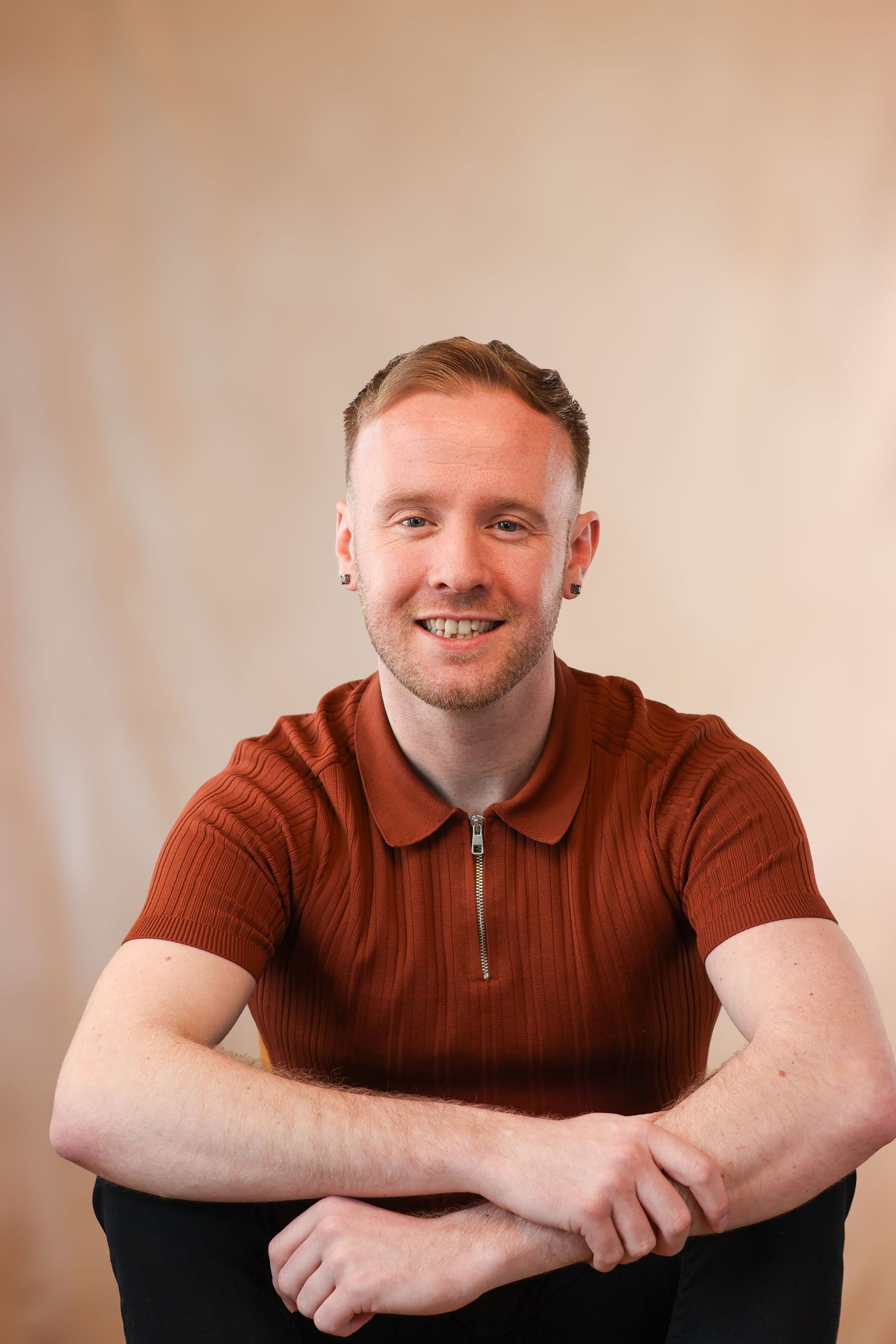 Man in rust-colored polo shirt smiling while seated in casual portrait pose.