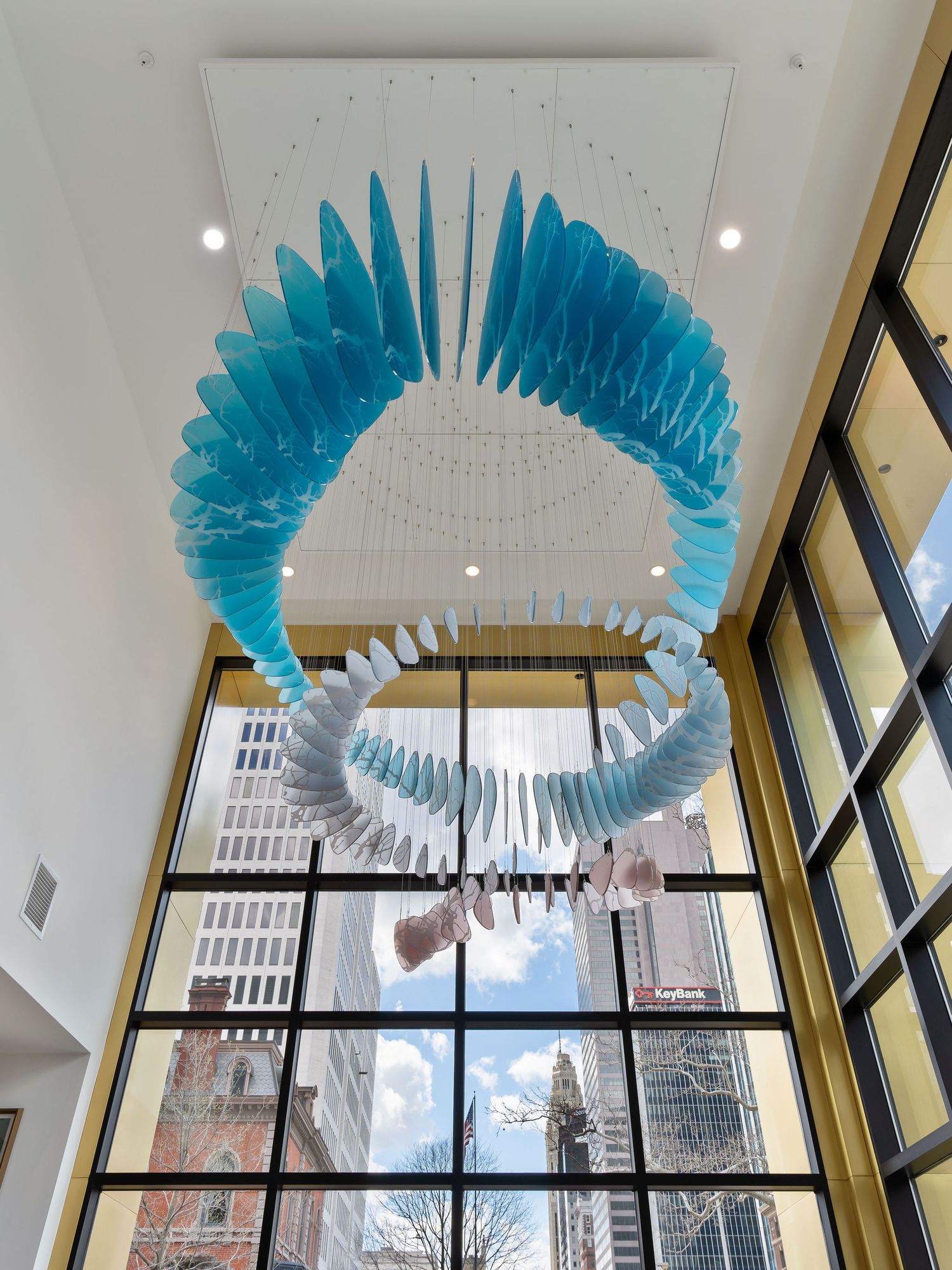 A circular blue and white art installation hangs from the ceiling in front of large windows in a modern apartment atrium in Columbus, Ohio.