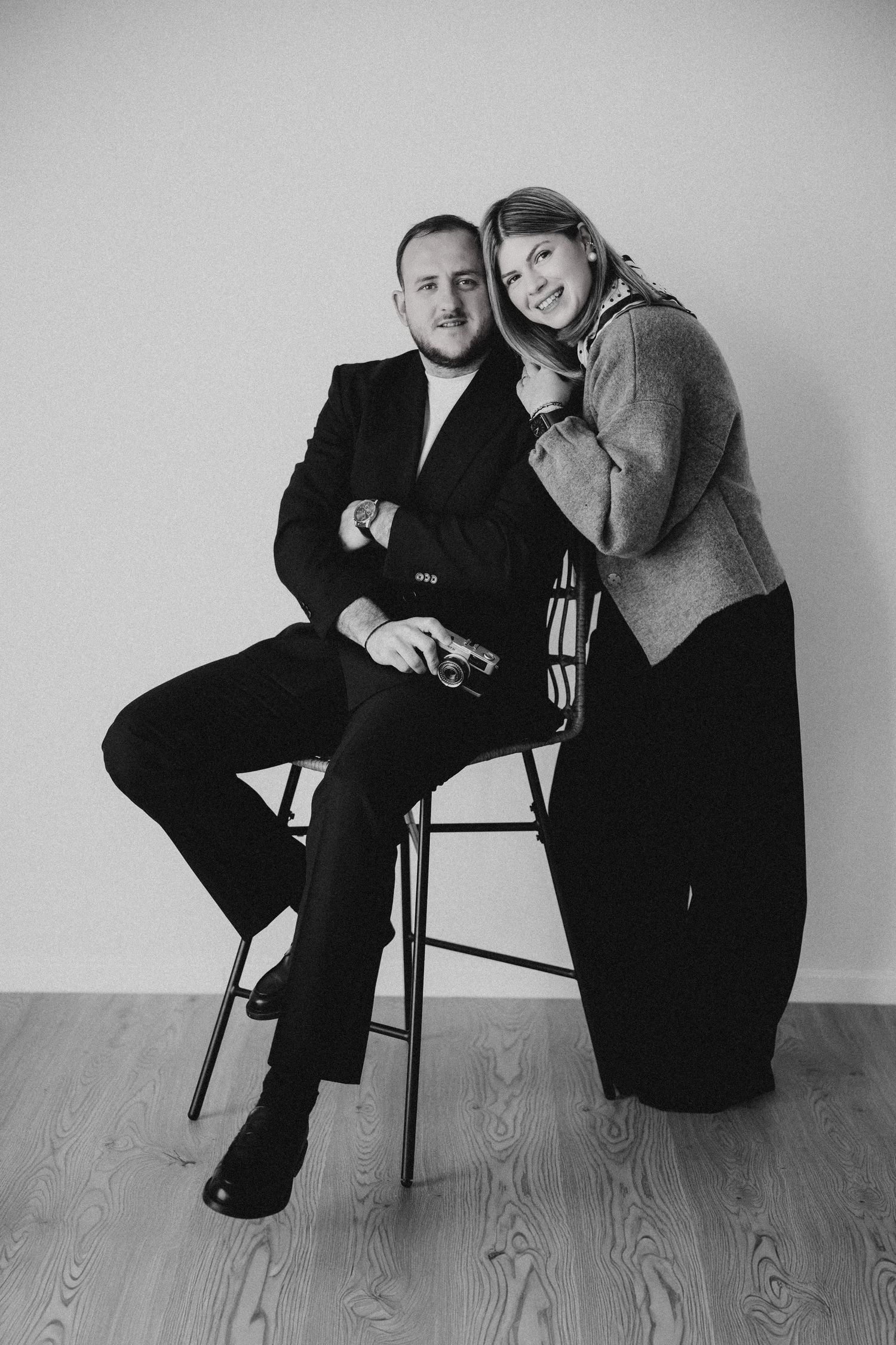 Black and white studio portrait of two people in dark clothing holding cameras.