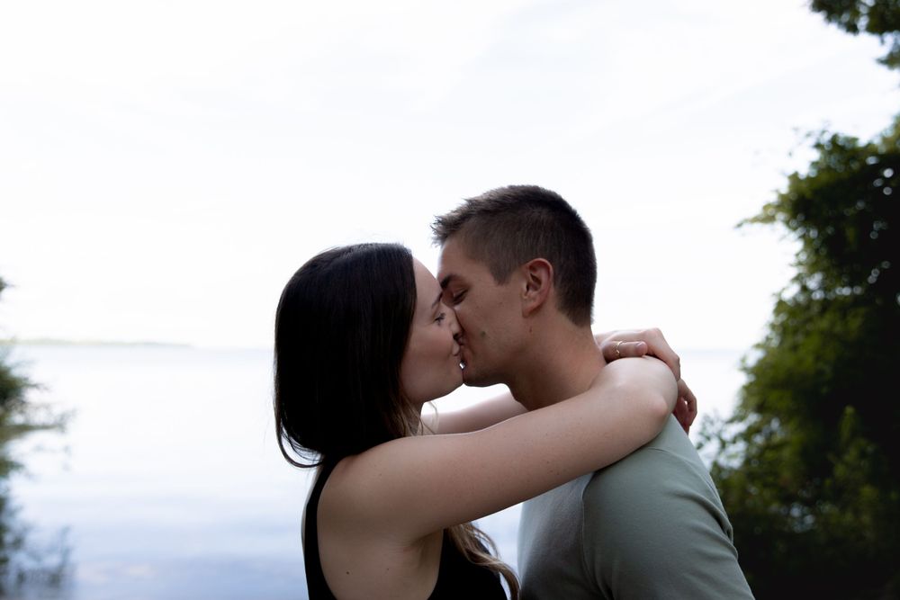 An intimate moment captured between a couple sharing a kiss against a cloudy sky backdrop.