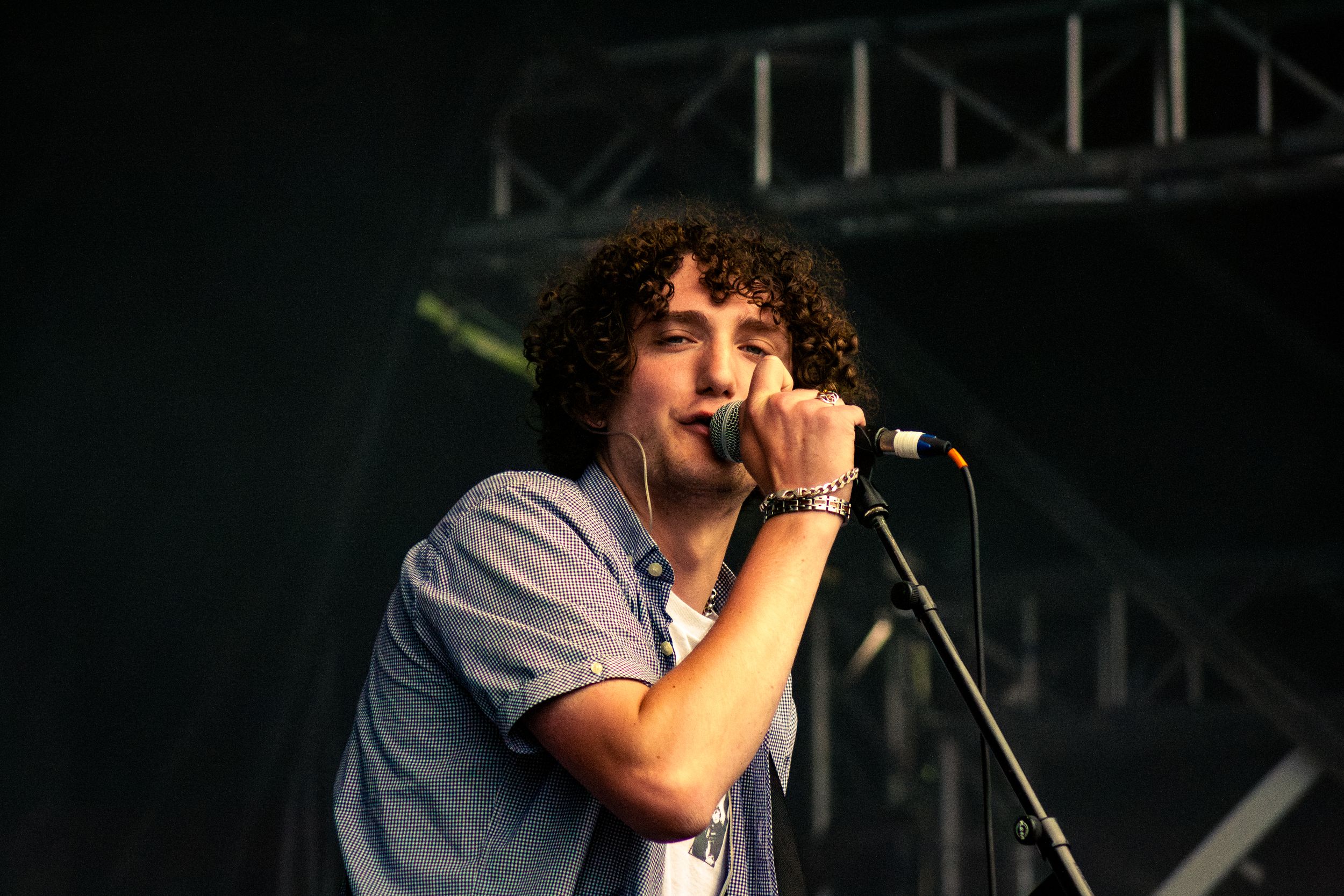 Singer performs with microphone on dark stage with industrial lighting setup.
