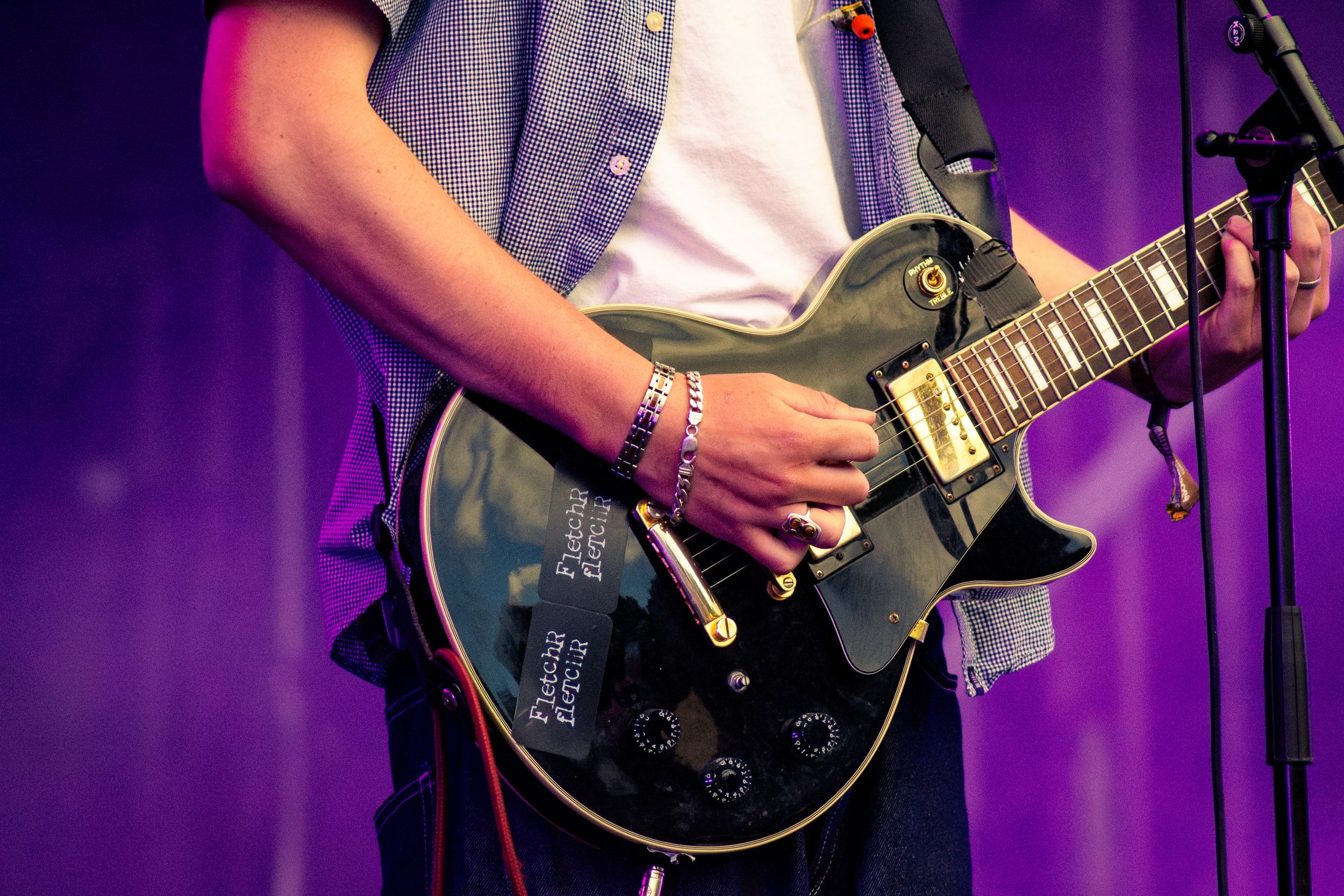 Close-up of guitarist playing black Les Paul electric guitar against purple stage lighting.