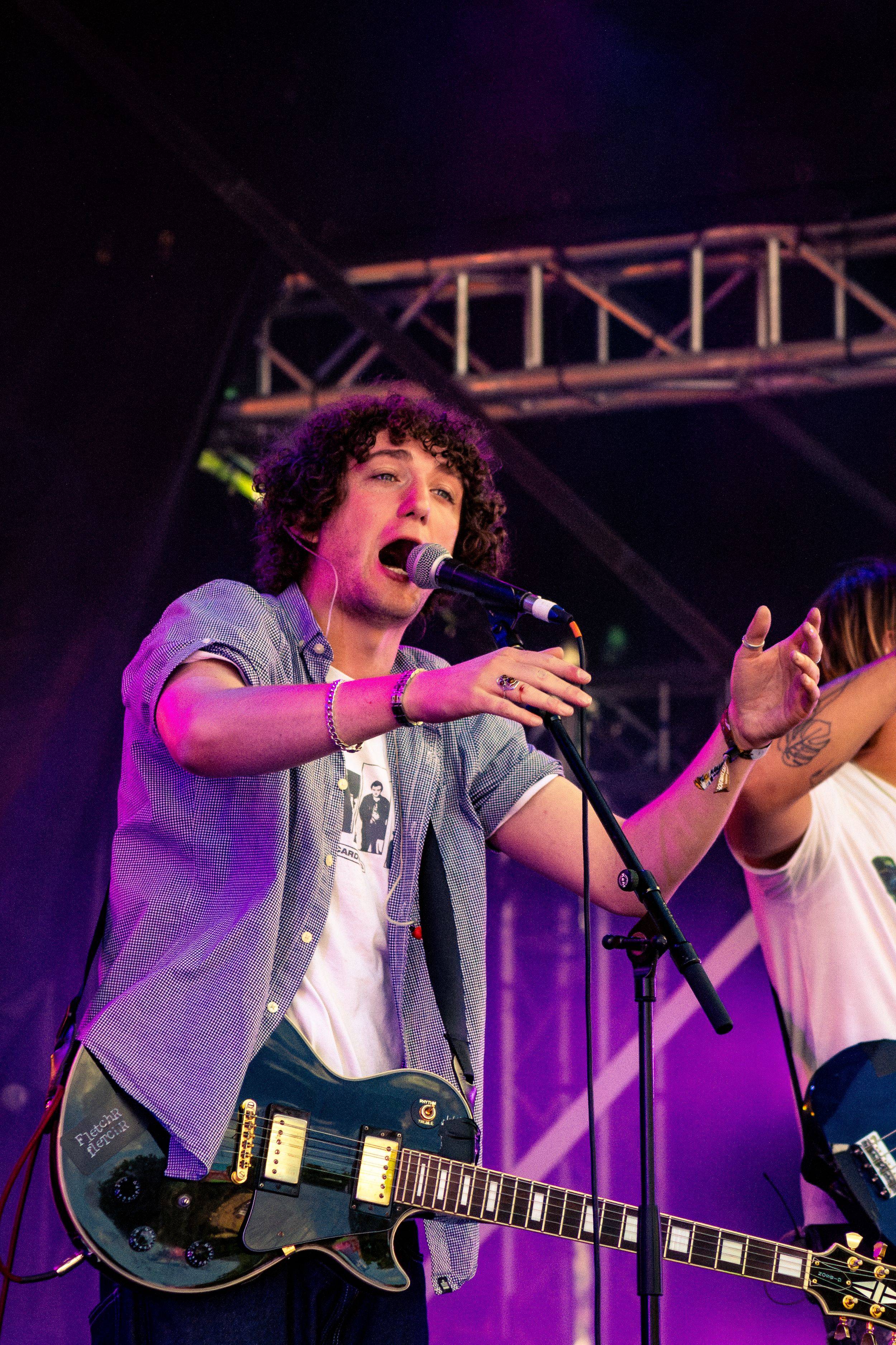 Musician performing passionately with an electric guitar wearing a denim jacket under purple stage lights.