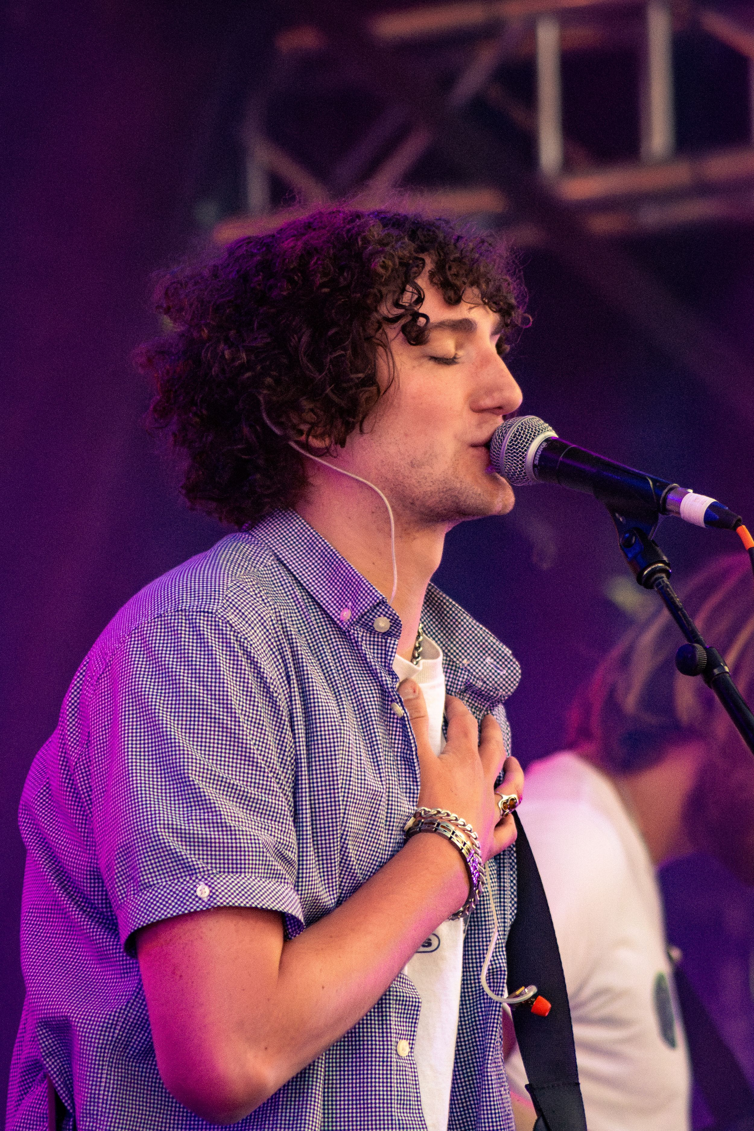 Singer performing with emotion in checkered shirt under purple stage lighting.