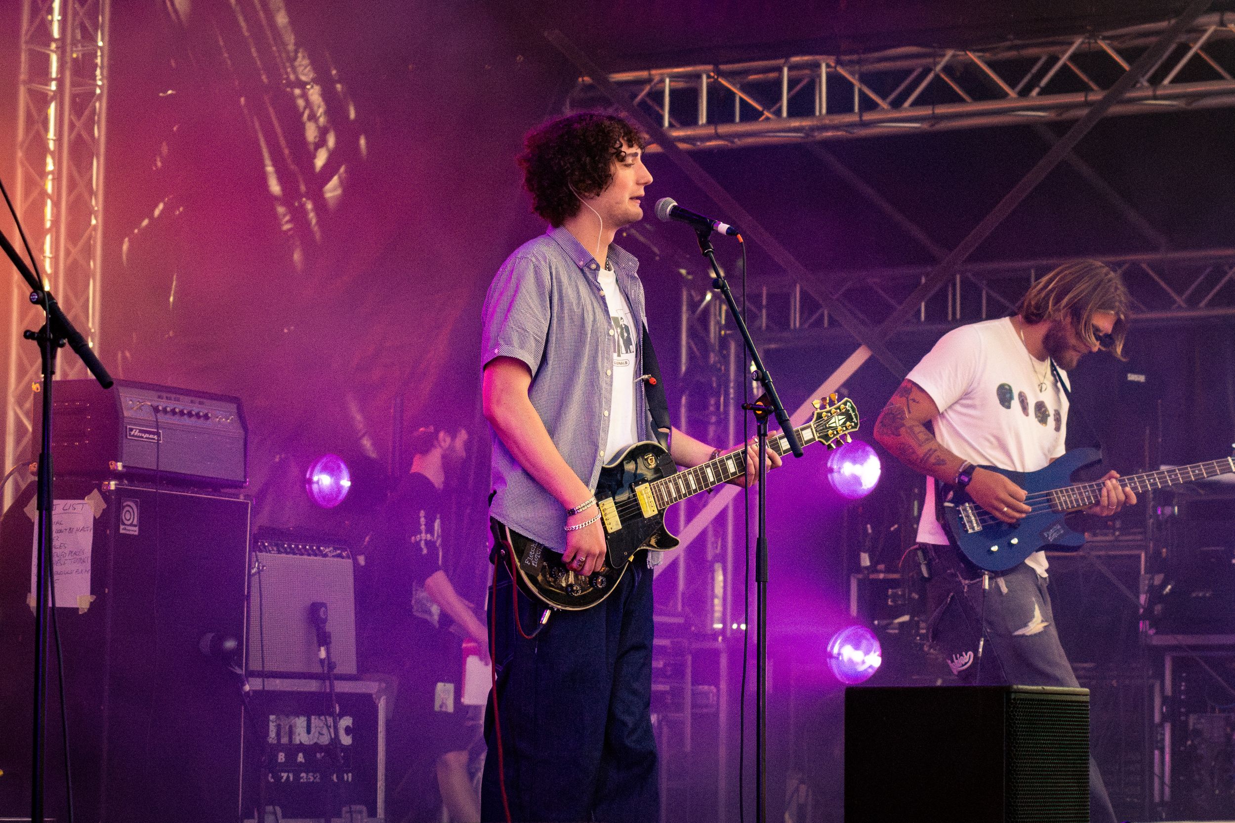 Band performing on stage with guitars and amplifiers under purple concert lighting.