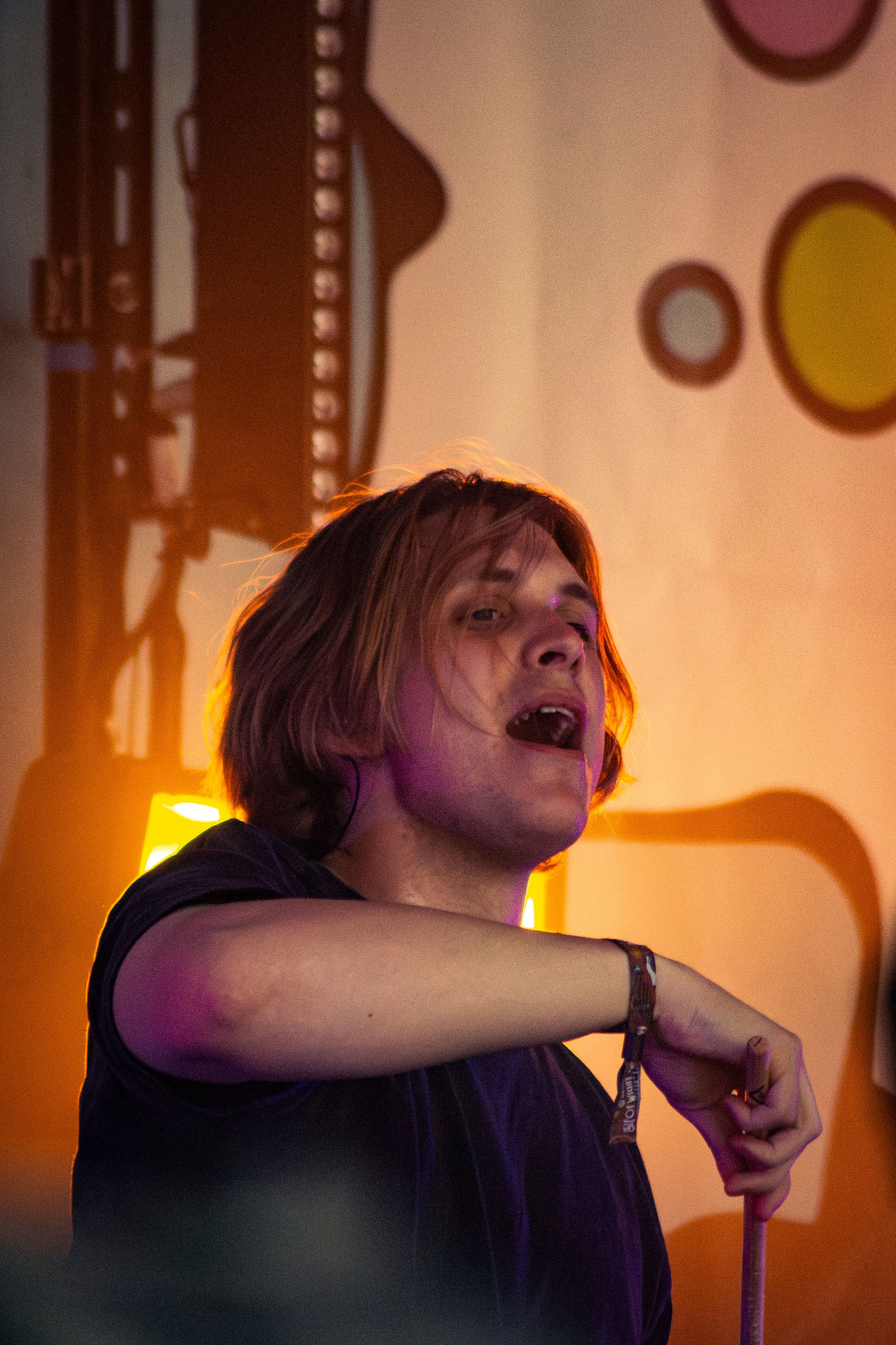 Singer performing passionately on stage with dramatic orange backlighting and circular wall decorations.