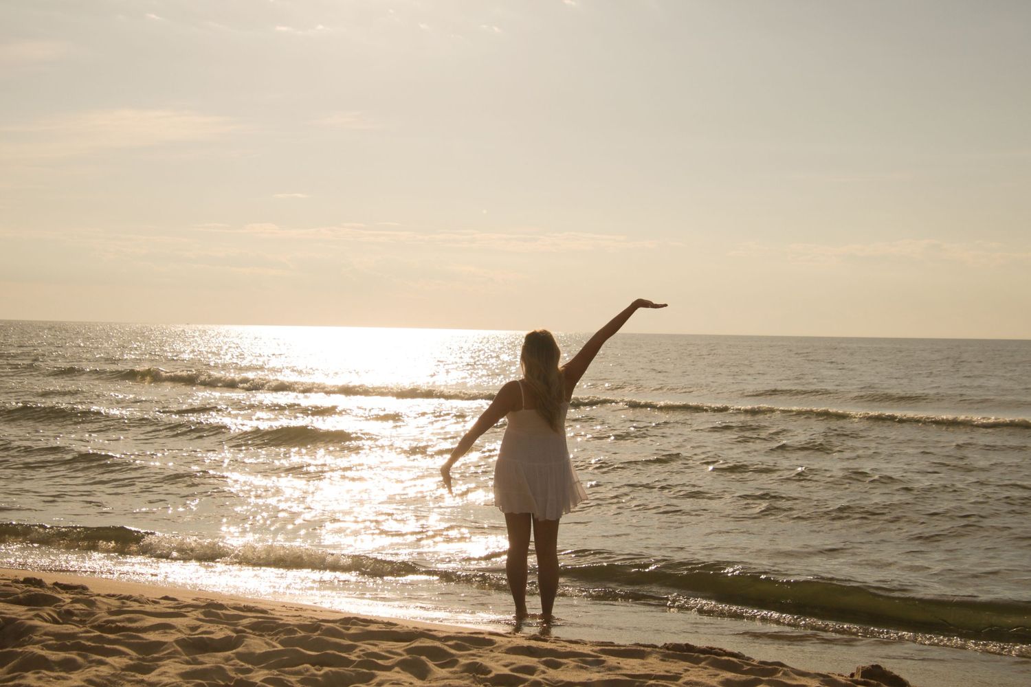 Silhouetted figure with arms outstretched on beach at golden sunset.