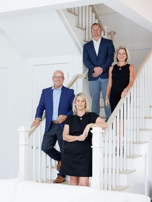 Professional real estate team of four posing on elegant white staircase.