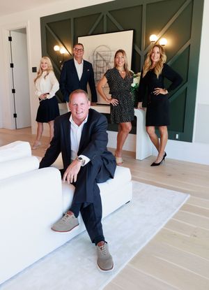 Professional real estate team of five posing in modern luxury home interior.