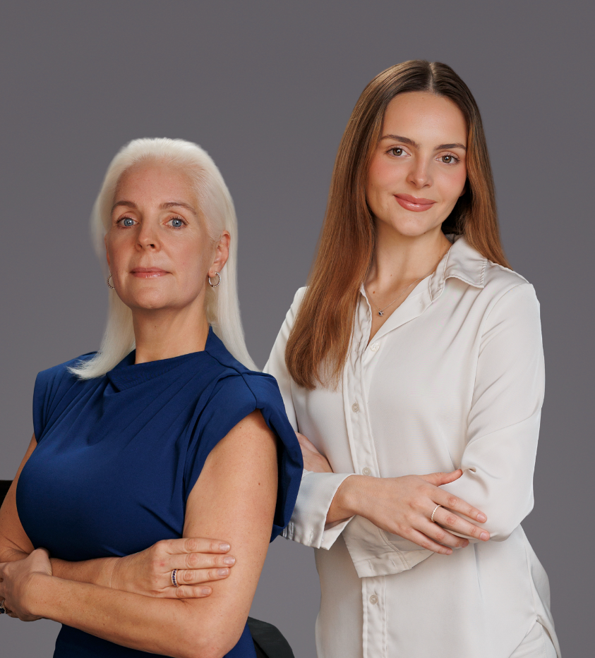 Two professional women posing confidently with arms crossed against a gray background.