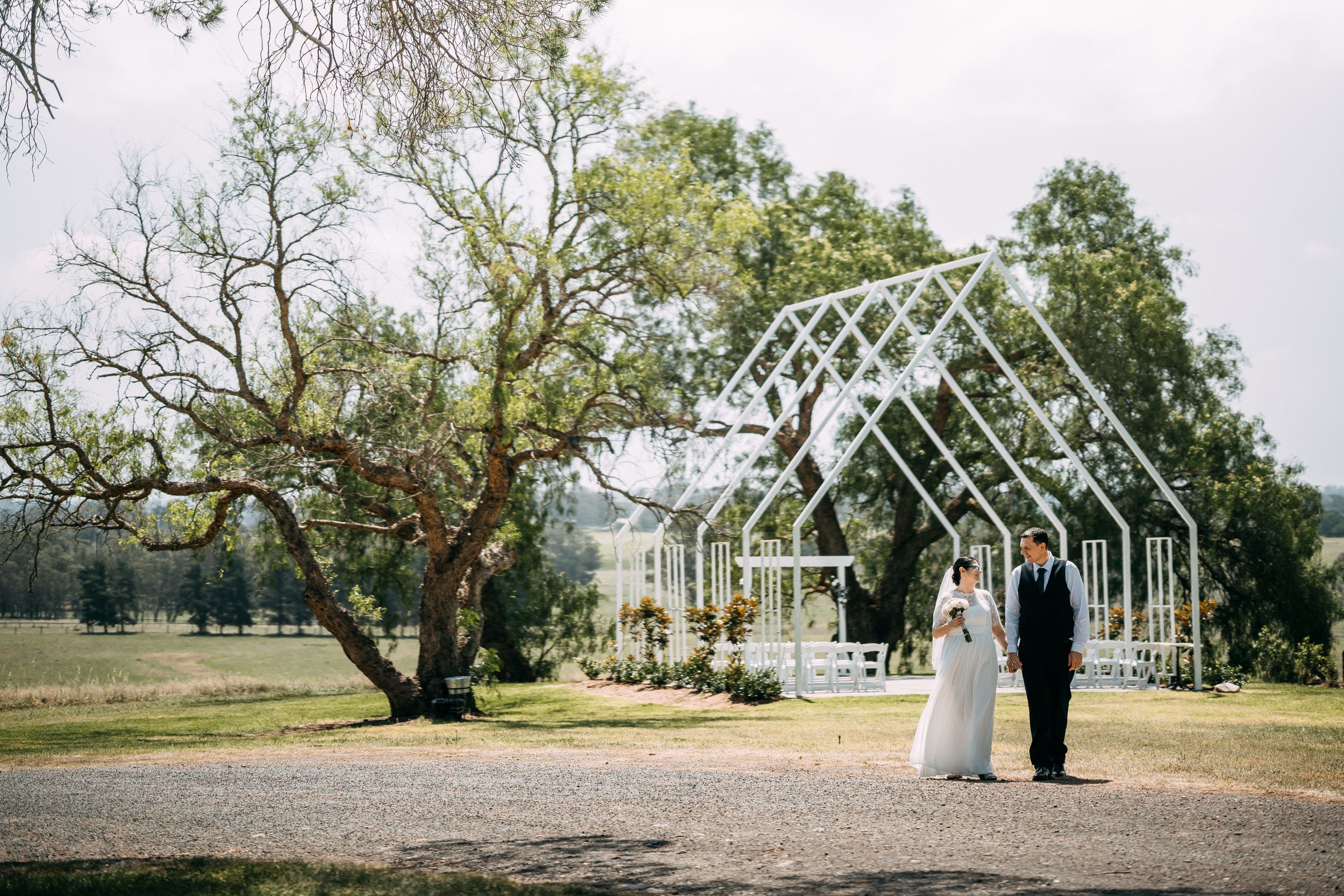 Wedding ceremony setup under a transparent greenhouse structure with natural woodland backdrop.