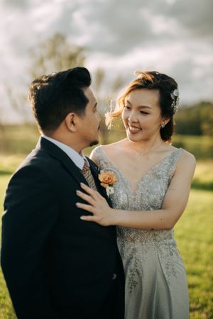 A couple shares an intimate moment in a sunlit field wearing formal attire.
