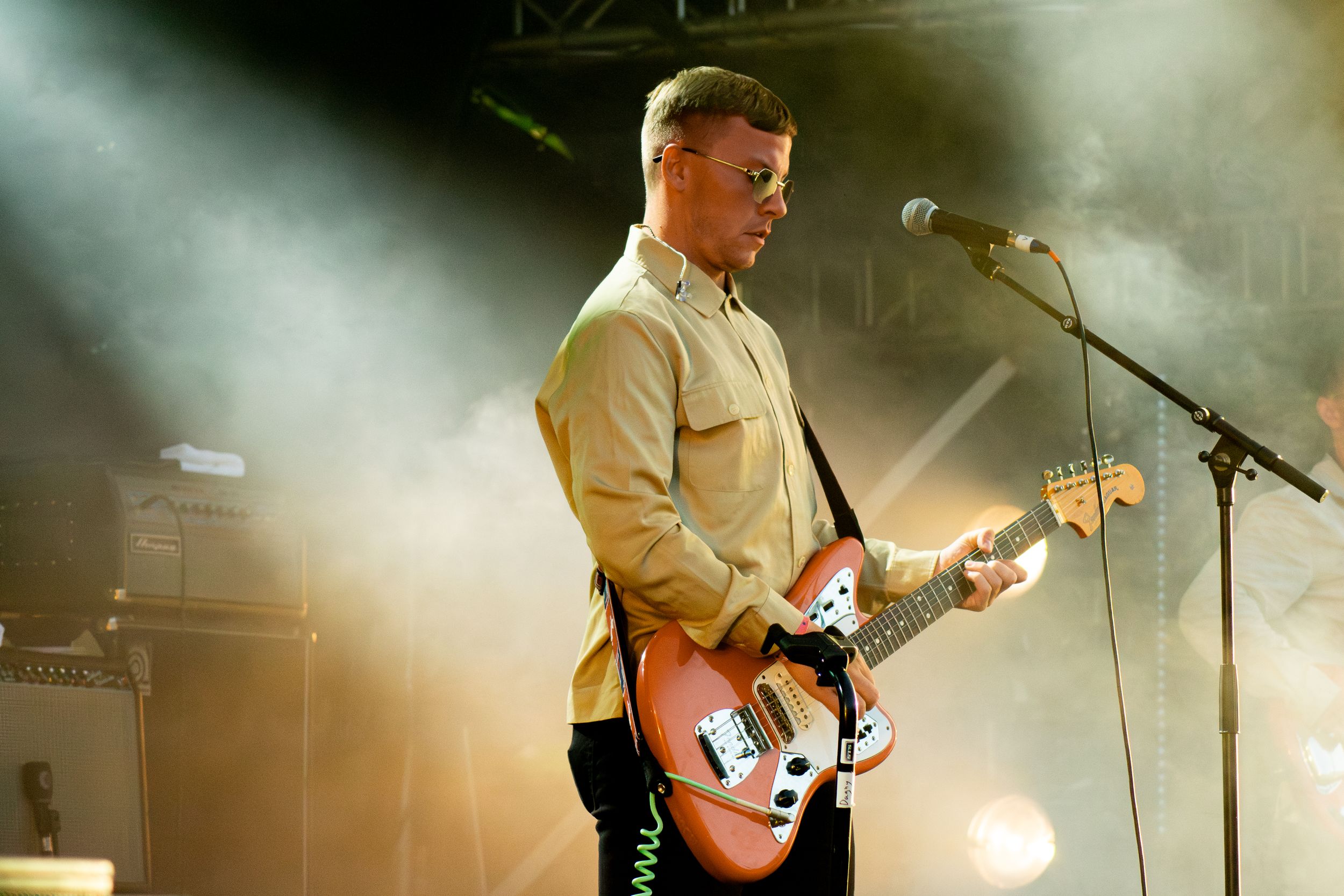Performer plays orange electric guitar on stage with dramatic backlighting and smoke effects.