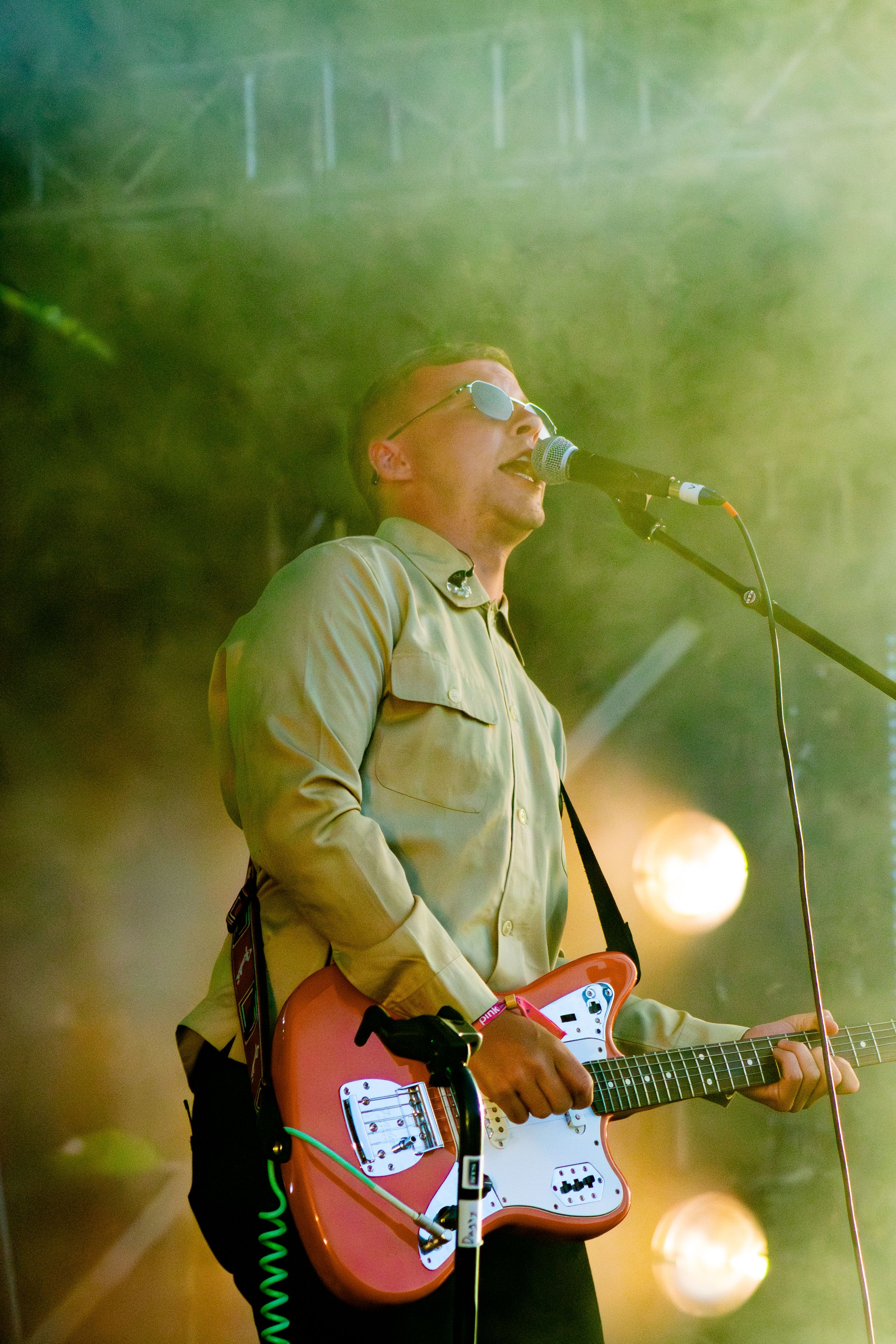 Guitarist performs with orange electric guitar in atmospheric green-tinted stage lighting.
