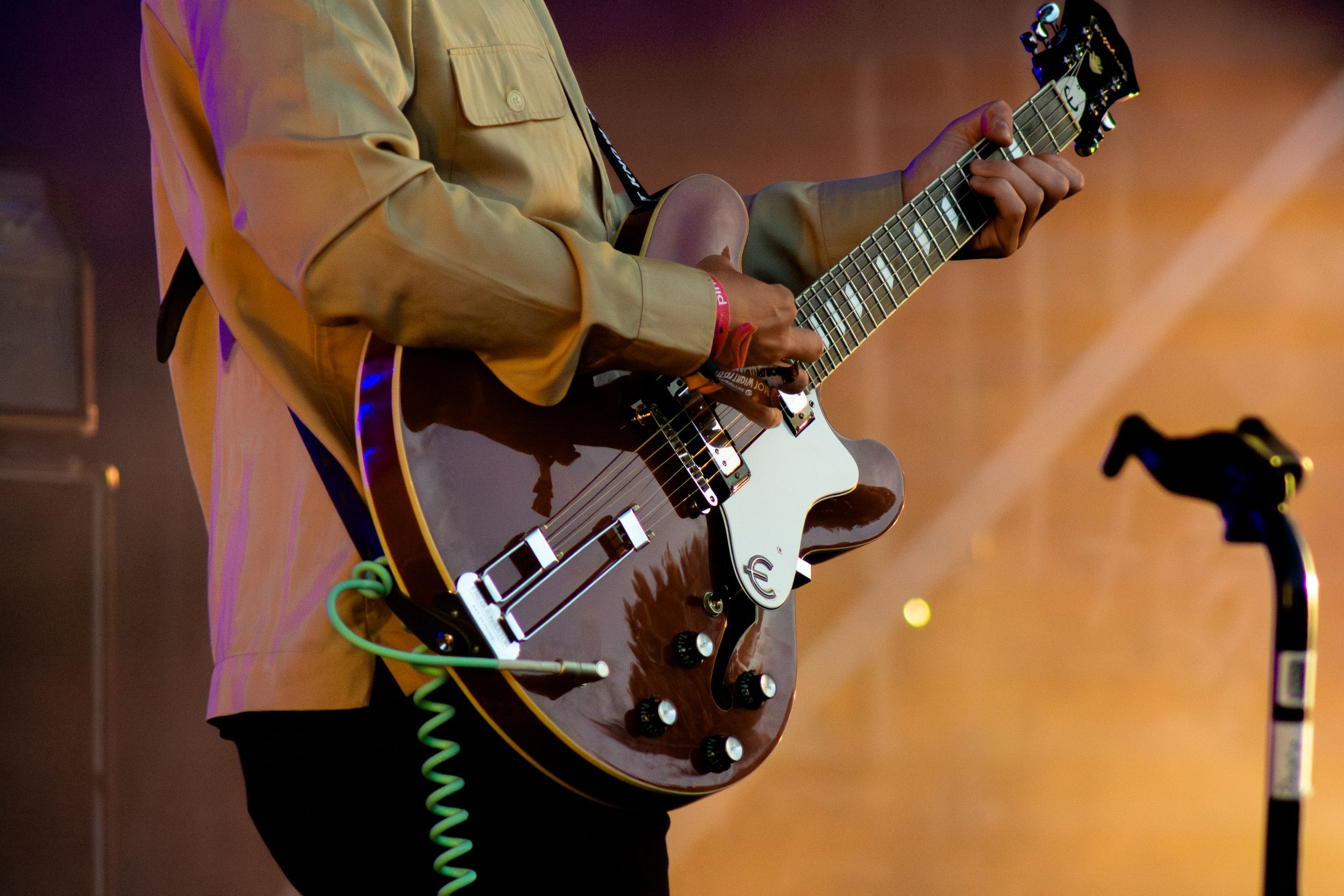 Close-up shot of musician playing brown electric guitar with coiled cable visible.