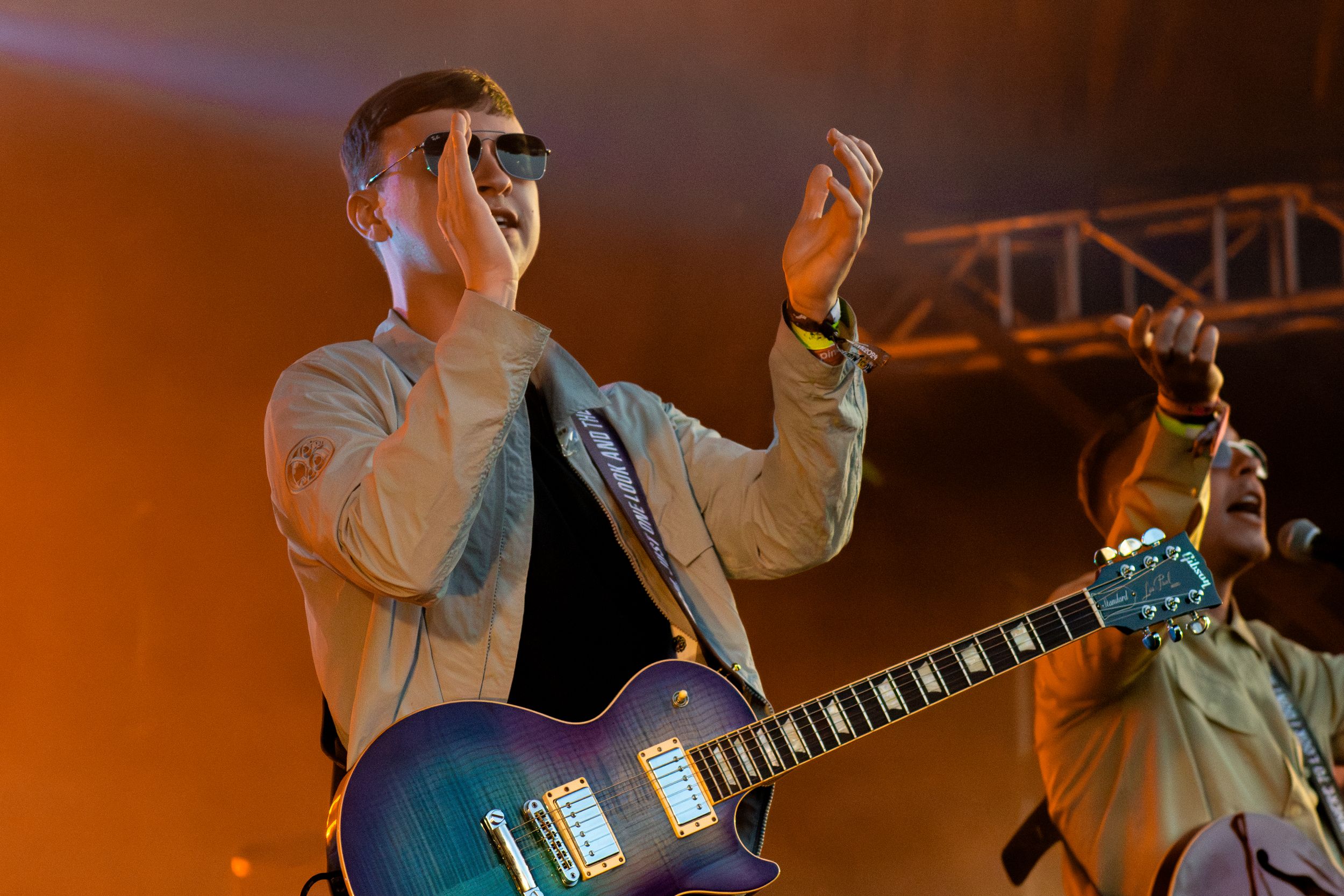 Performer with guitar engages audience under dramatic orange stage lighting and metal truss rigging.