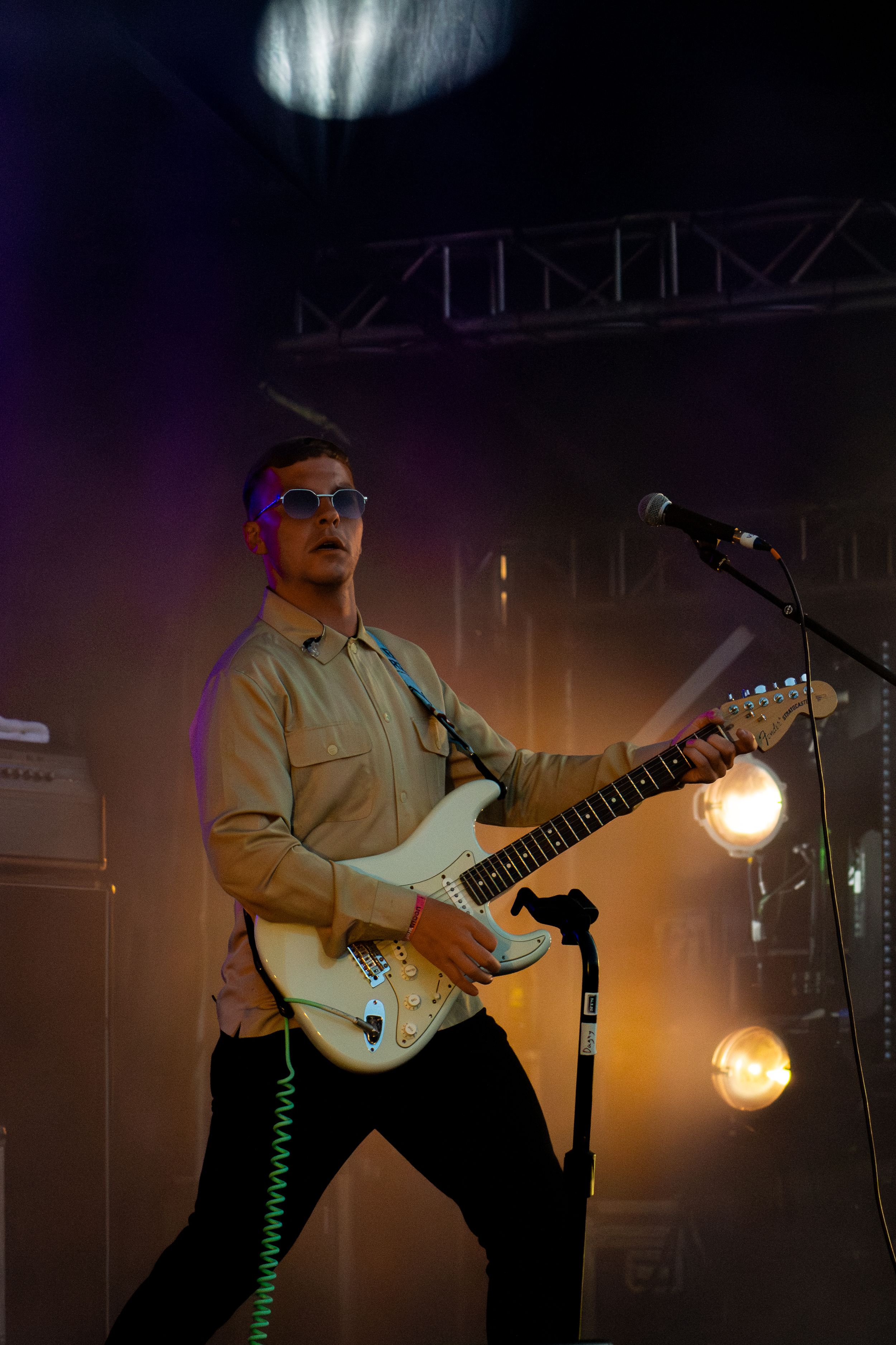 Guitarist performs with white electric guitar under dramatic stage lighting and spotlights.