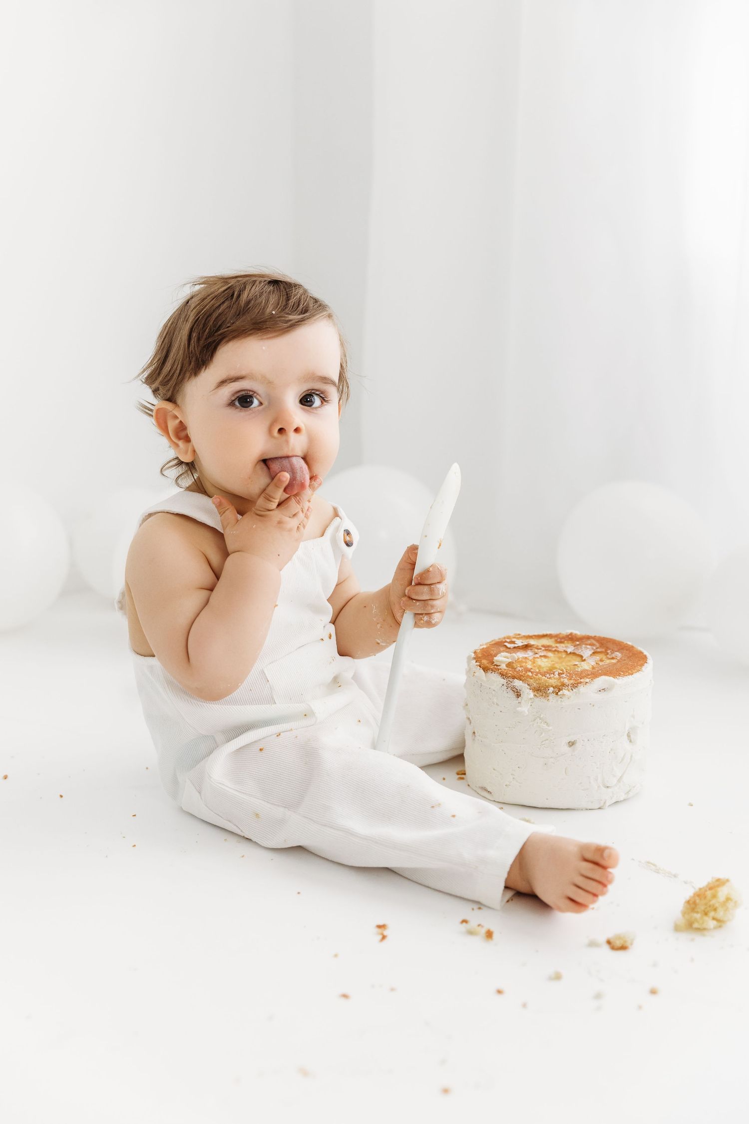 One Year Old Baby Boy Eating Cake with a big plastic spoon, licking icing off fingers