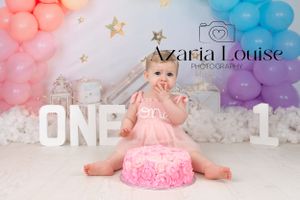 First birthday cake smash photo with white ONE letters, pink and blue balloon arch, and pink frosted cake.