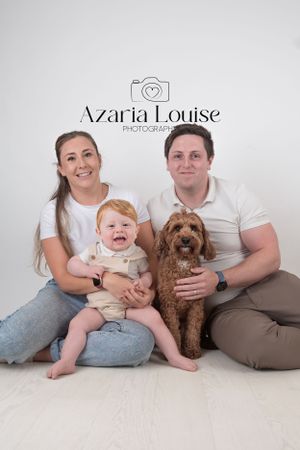 Family portrait with a brown goldendoodle dog sitting together on a white backdrop with Azaria Louise Photography logo.