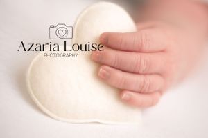 A tiny baby hand rests gently on a soft white heart-shaped surface in a dreamy, pastel-toned photograph.