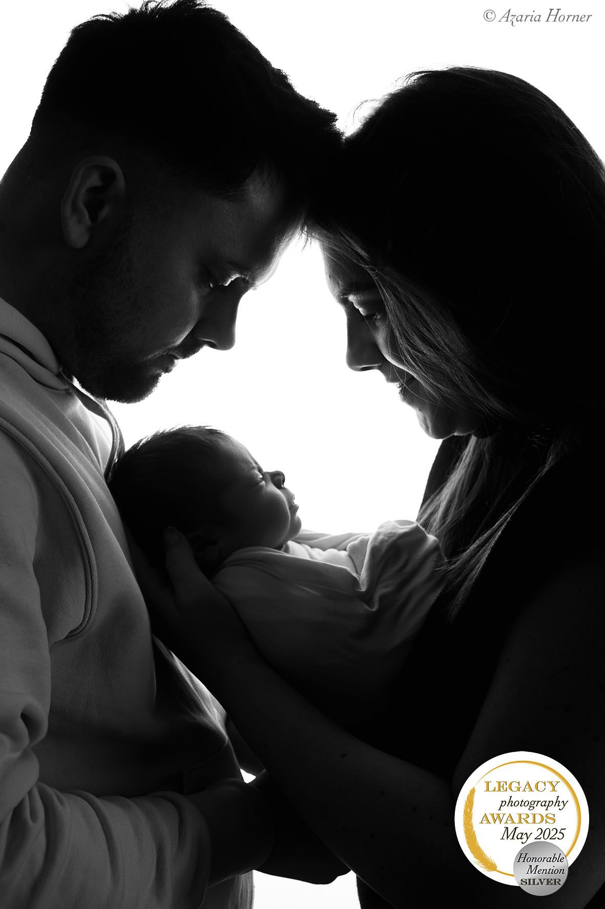 Black and white silhouette of parents tenderly cradling their newborn baby in an intimate family portrait.