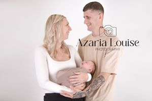A couple shares a tender moment while cradling their newborn baby against a white studio backdrop.