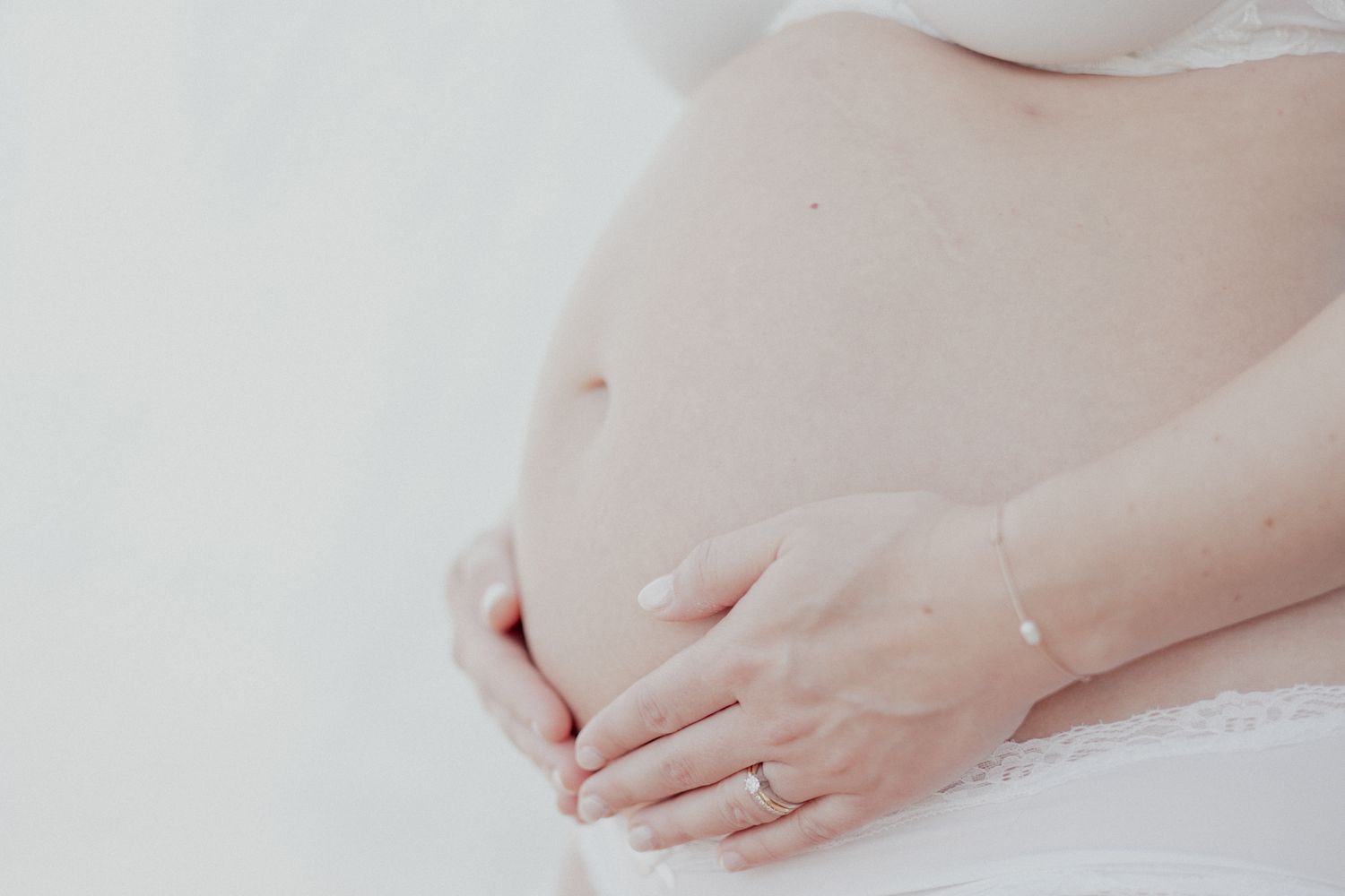 Close up of hands gently cradling a pregnant belly in soft natural light.