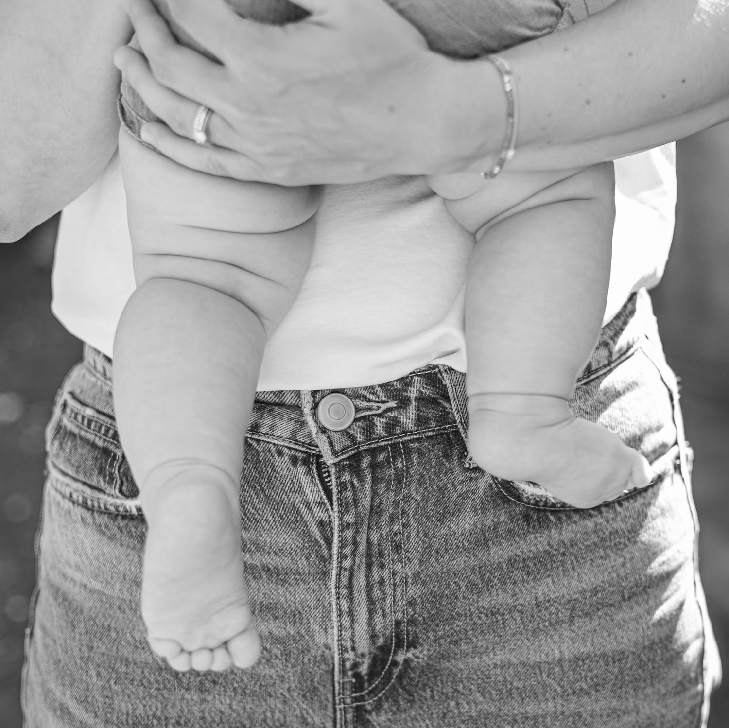 Black and white photo of baby legs being held against denim jeans.